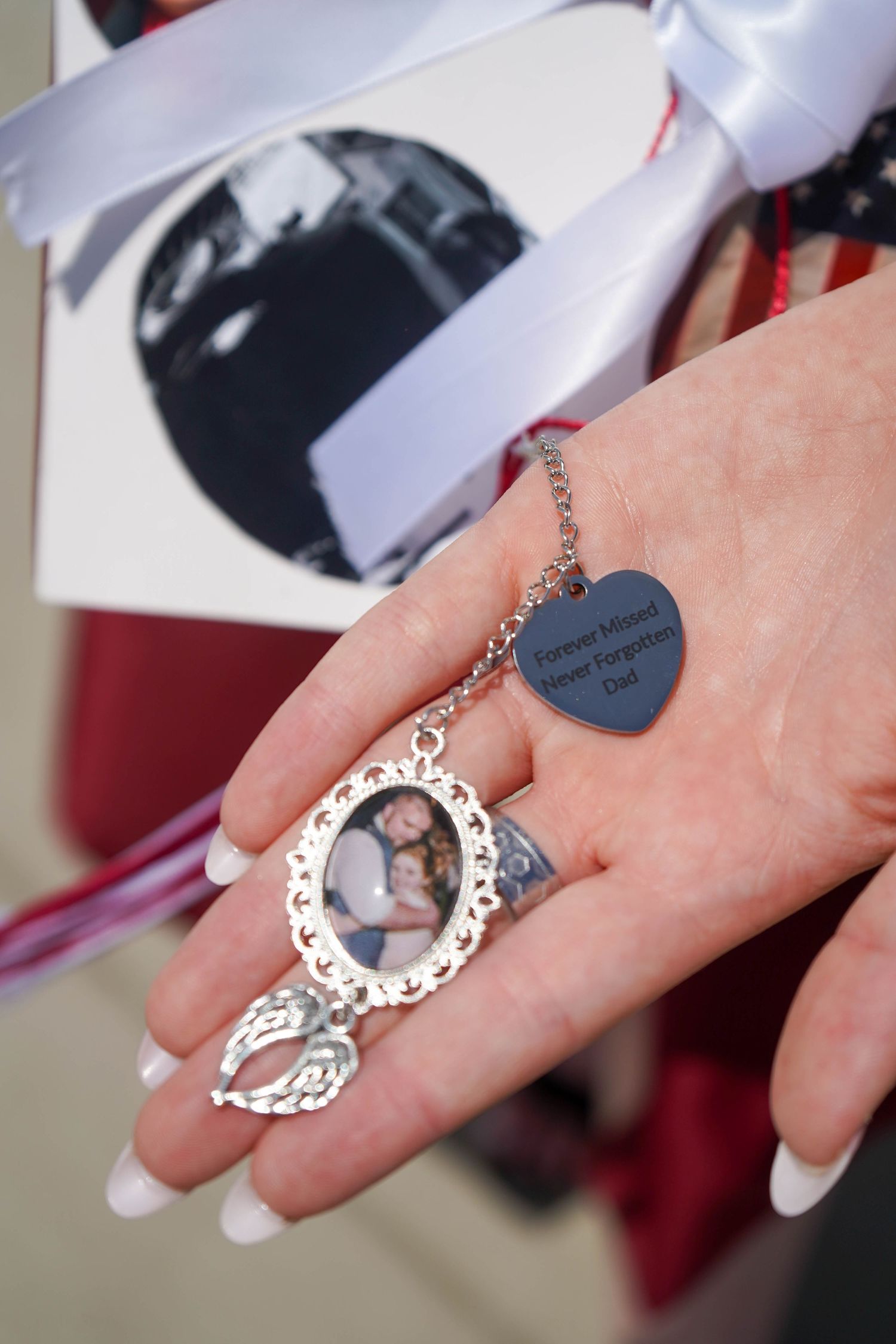 Hand holding a memorial charm with photo and heart pendant engraved Never Forgotten Dad.