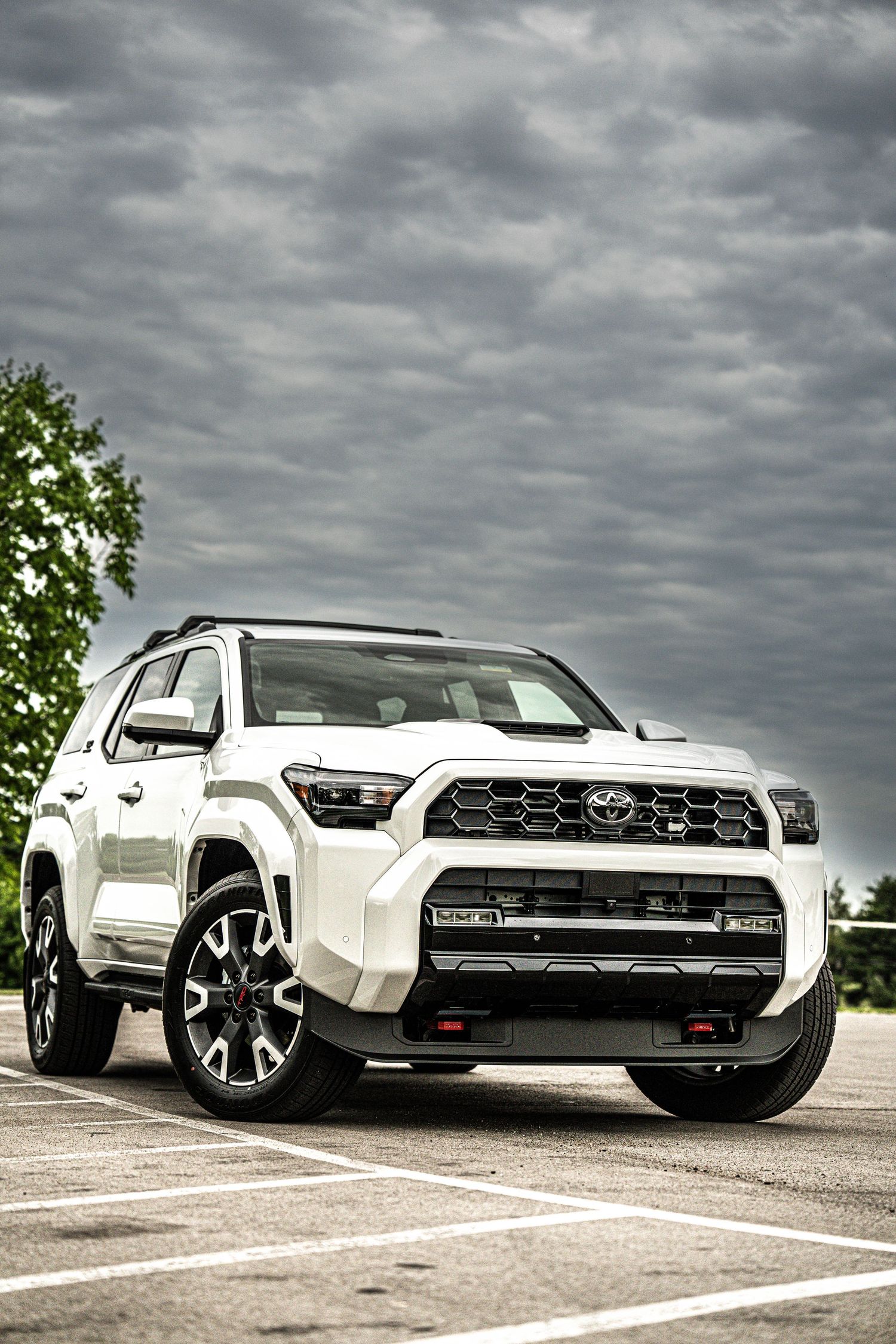 White Toyota 4Runner TRD Pro SUV parked under dramatic cloudy sky, front three-quarter view showcasing bold grille and off-road styling.
