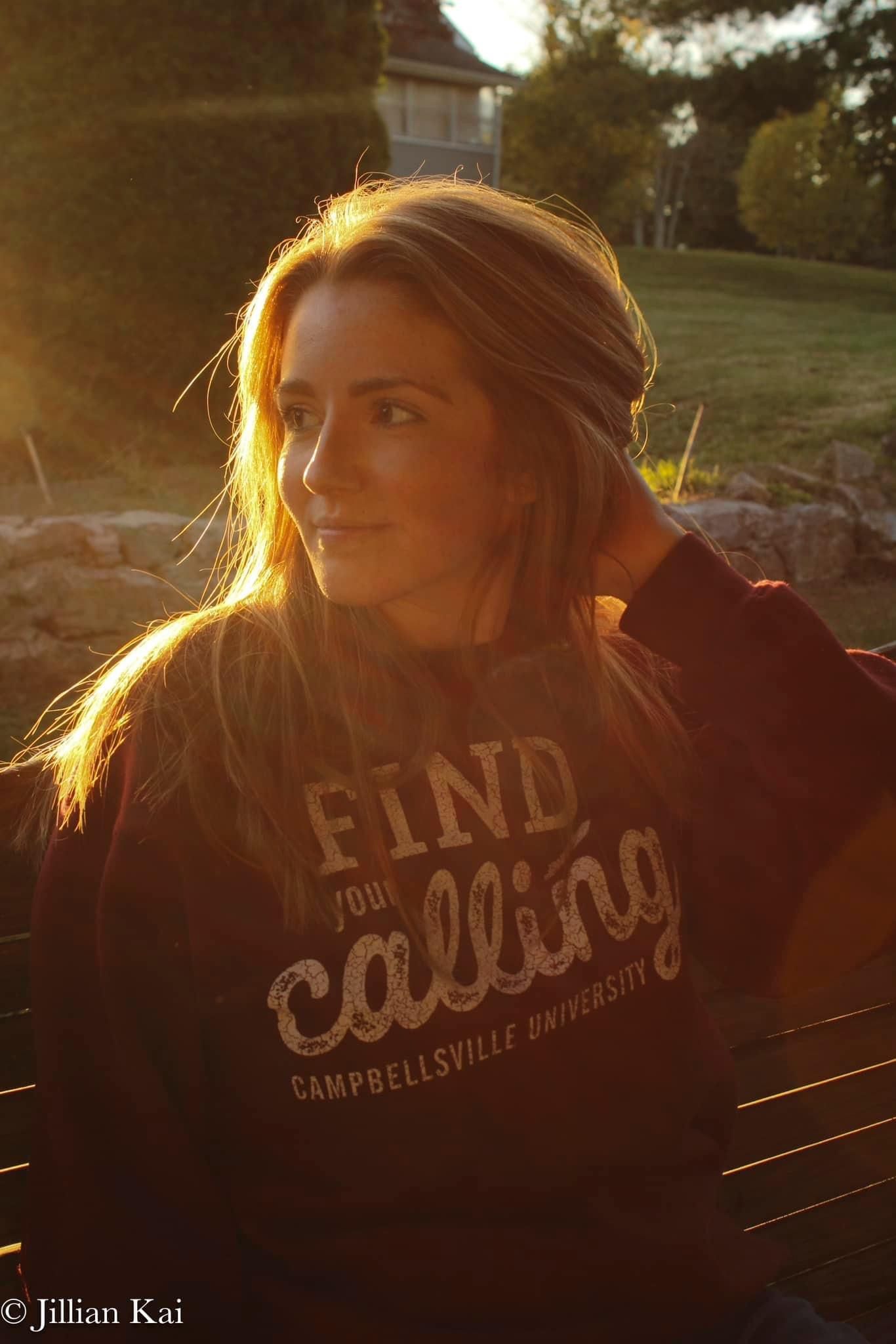 Young woman in Campbellsville University sweatshirt bathed in golden sunset light.