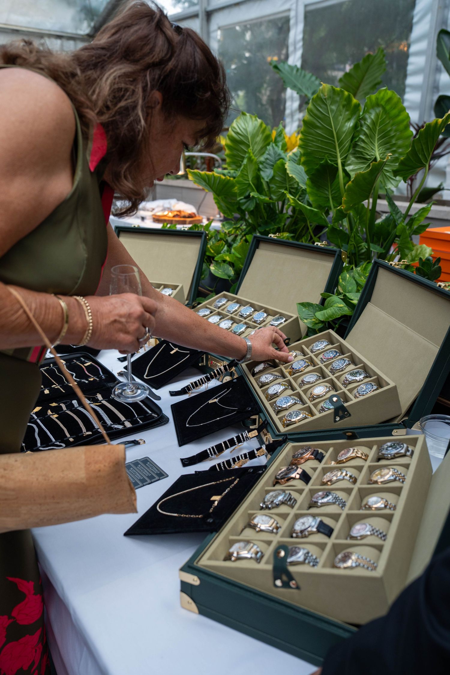 Woman browsing luxury watches and jewelry displayed in velvet cases at an outdoor market or event.