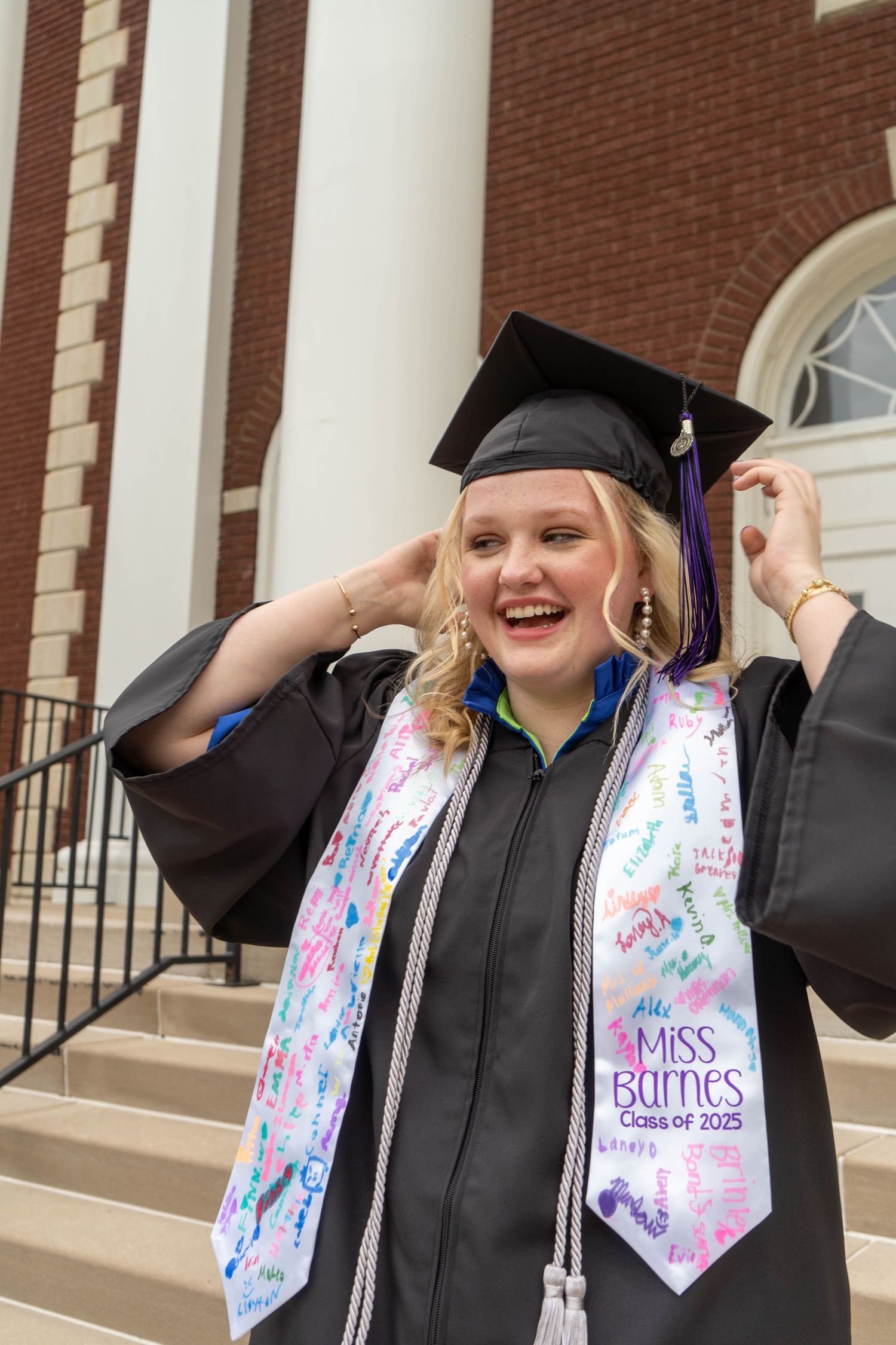 Laughing graduate in cap and gown wearing Miss Barnes Class of 2025 stole.