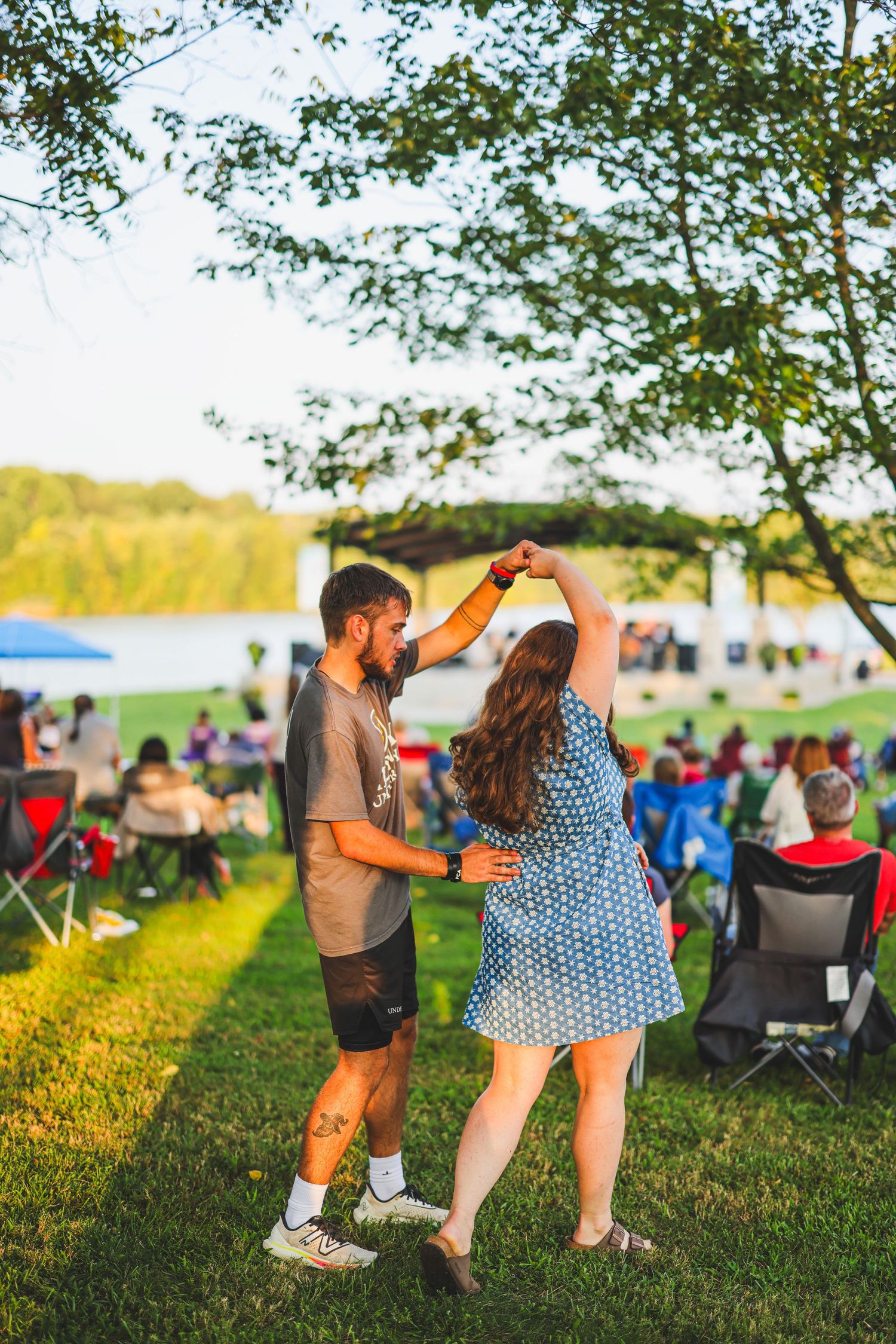 Couple dancing together on green lawn at outdoor summer concert event during golden hour sunset.