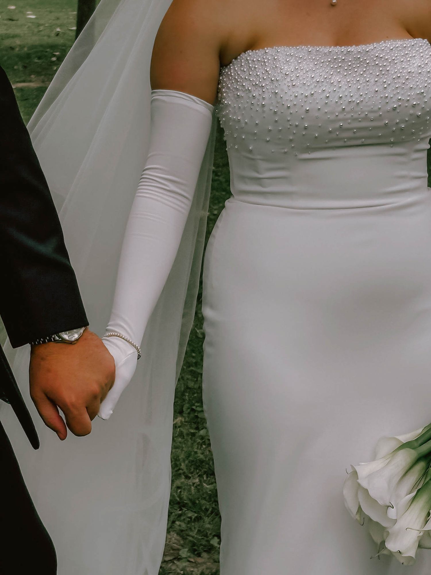 Close-up of bride in strapless pearl gown with white gloves holding hands with groom.
