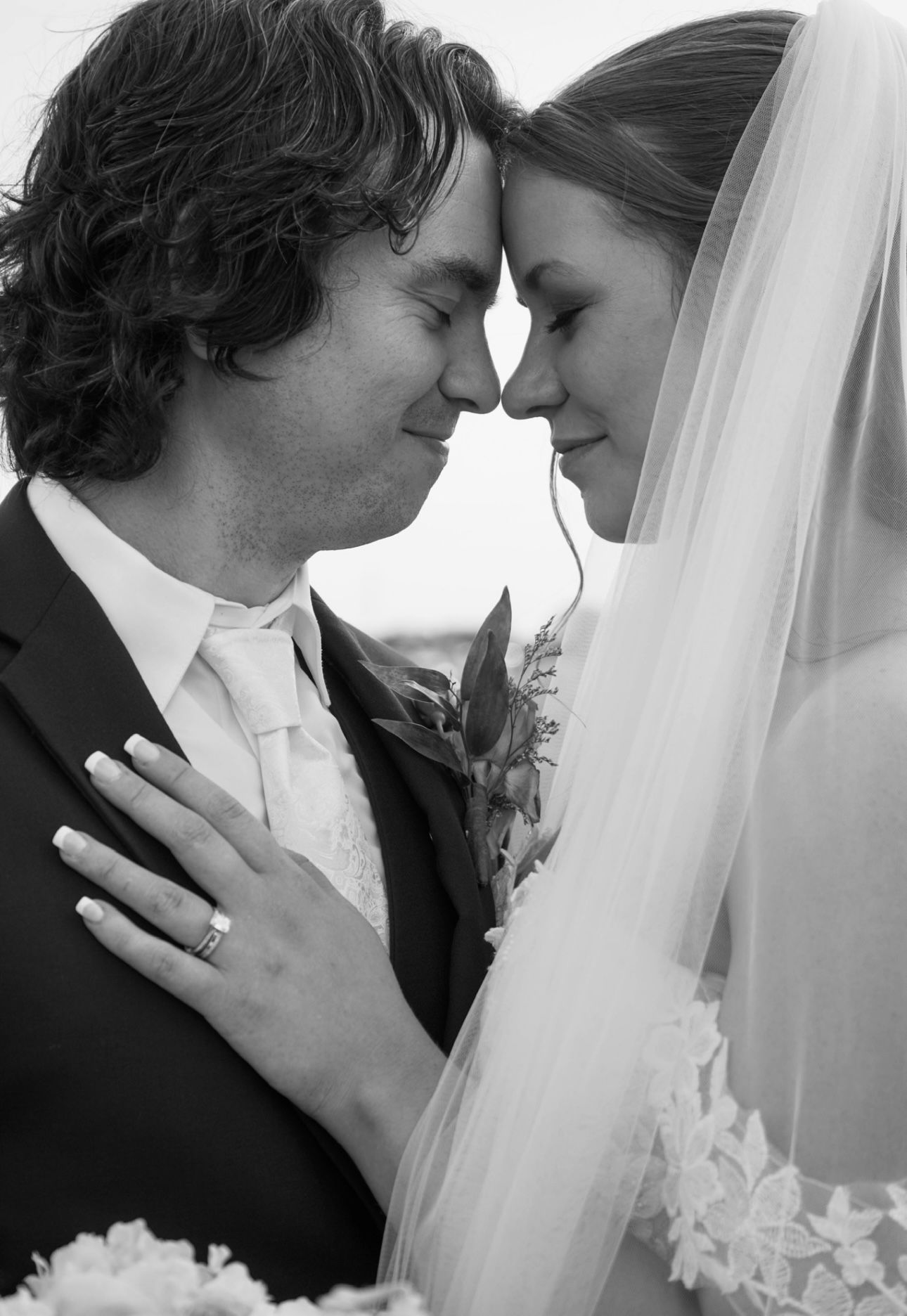 Black and white wedding photo of bride and groom touching foreheads romantically, bride wearing lace veil.