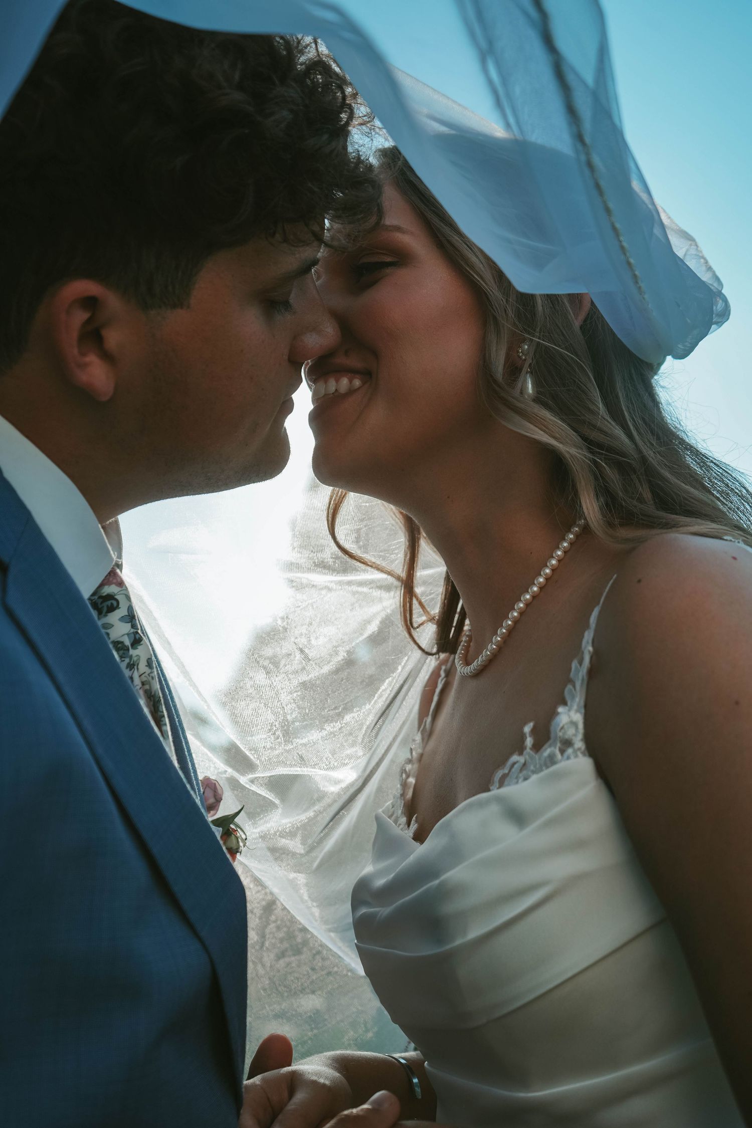 Bride and groom share a romantic almost-kiss under a flowing veil on their wedding day.