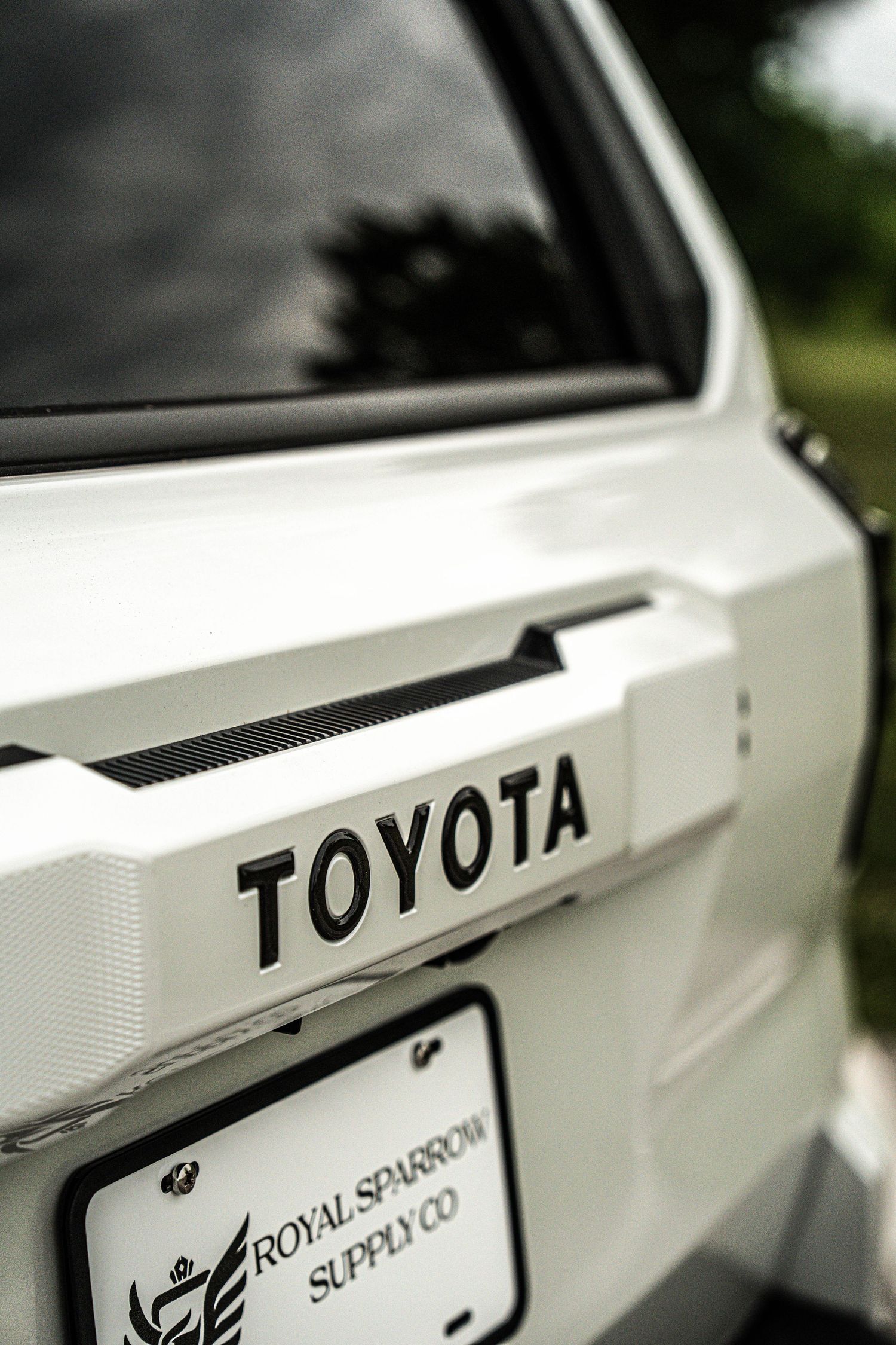 Close-up of a white Toyota truck rear badge with a Royal Sparrow Supply Co license plate frame.