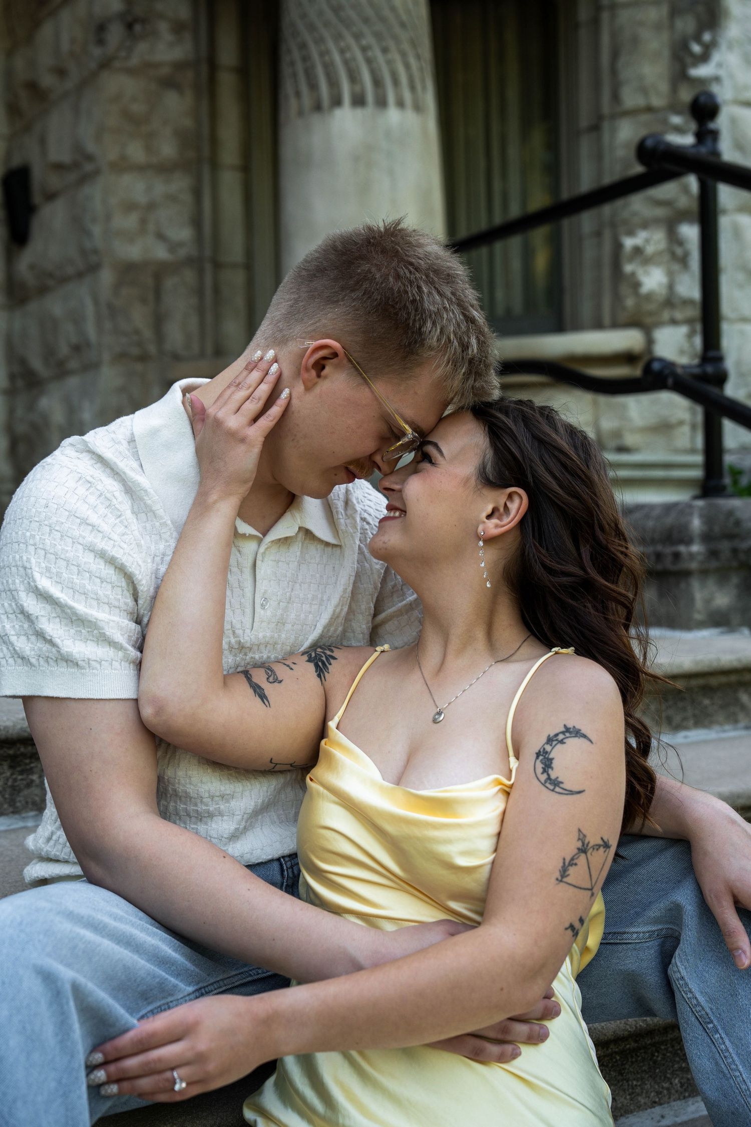 Couple sitting on stone steps, smiling and touching foreheads in a romantic moment.