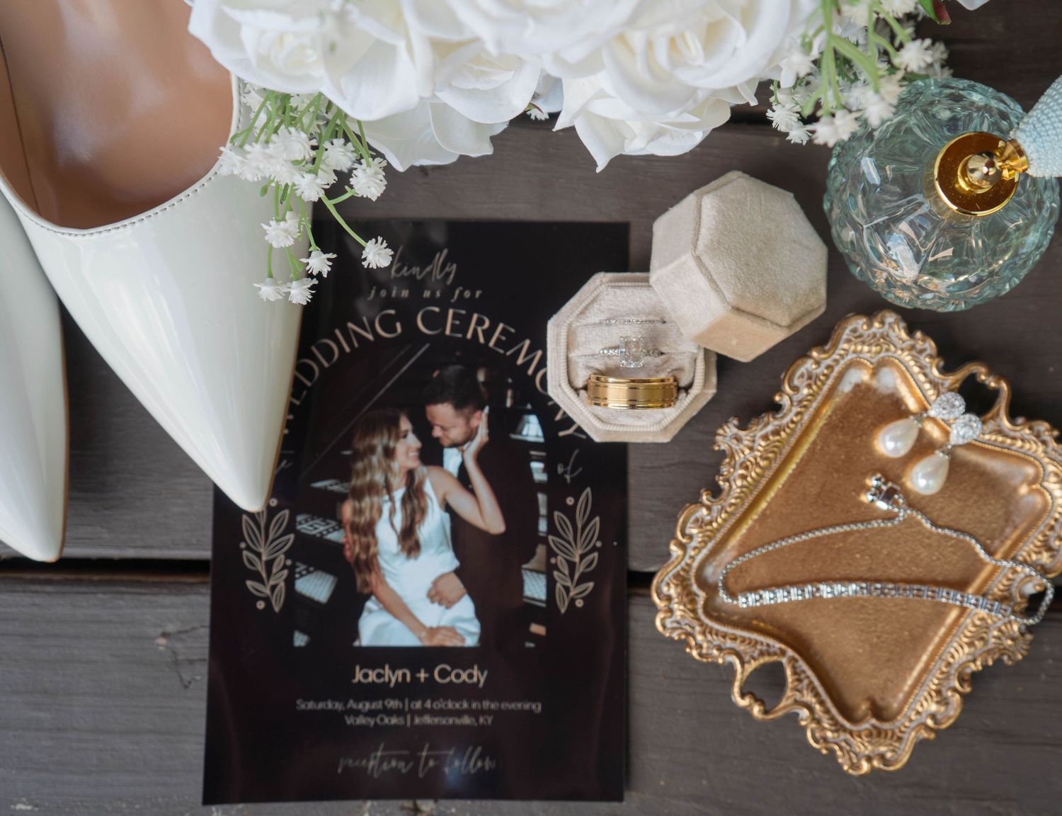 Wedding flat lay featuring ceremony program, bridal jewelry, rings, perfume, and white heels.