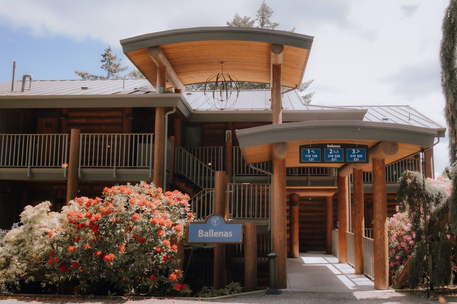 Modern wooden building entrance with Asian-inspired architecture and blooming pink flowers in the landscaping.