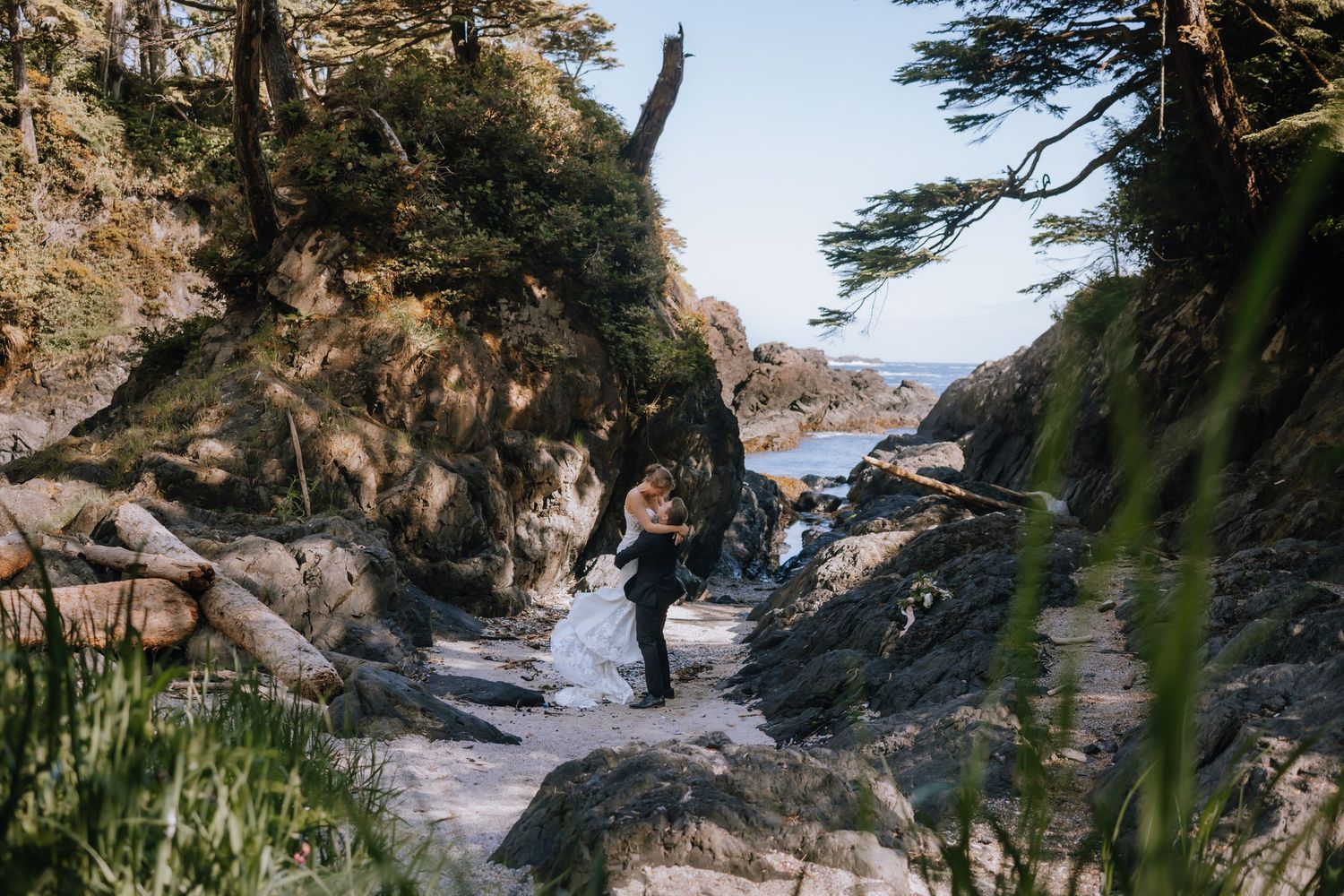 A couple embraces on a scenic rocky beach path surrounded by cliffs and trees along the coast at Black Rock Resort in Ucluelet