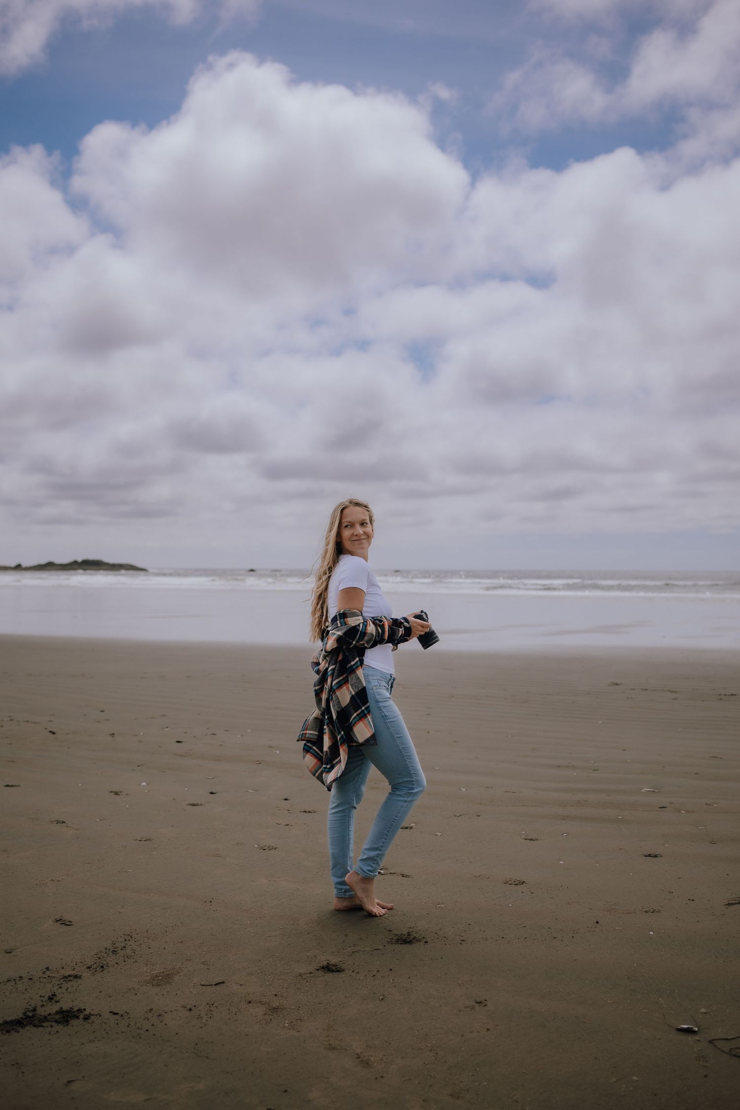 Photographer with camera captures seaside moments on a cloudy day at a sandy beach.