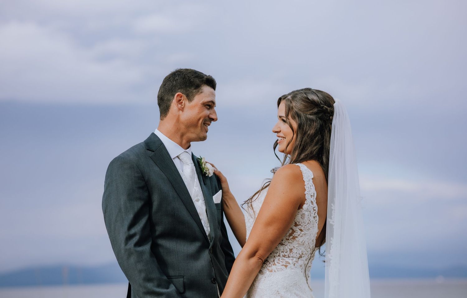 A couple in formal attire shares a romantic moment on a beach during their wedding photoshoot at sunset.