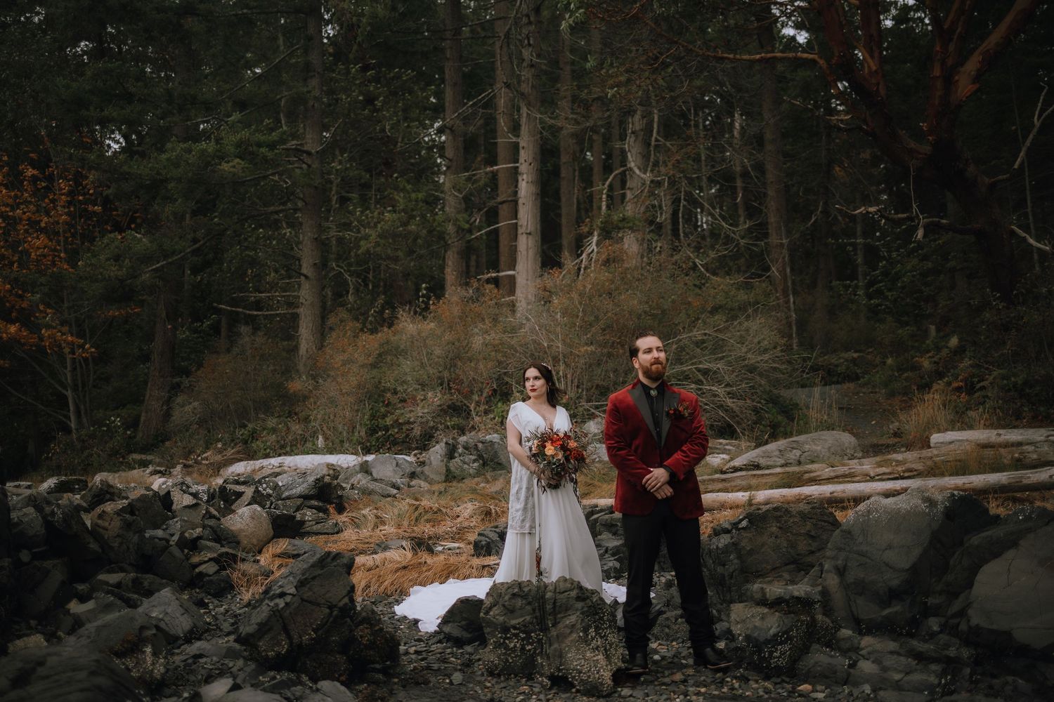 A couple stands on rocky terrain in a moody forest setting before their first look on their wedding day at Moorcroft Park, Nanoose Bay BC
