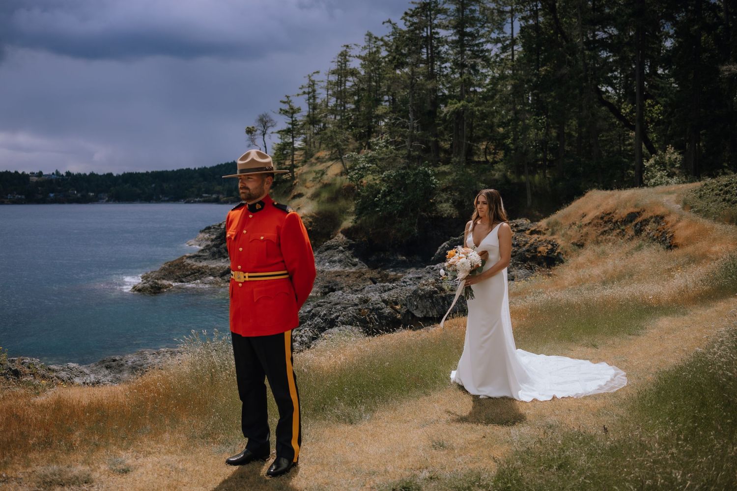 A wedding photo session overlooking a rugged Pacific Northwest coastline with evergreen trees and dramatic stormy sky.