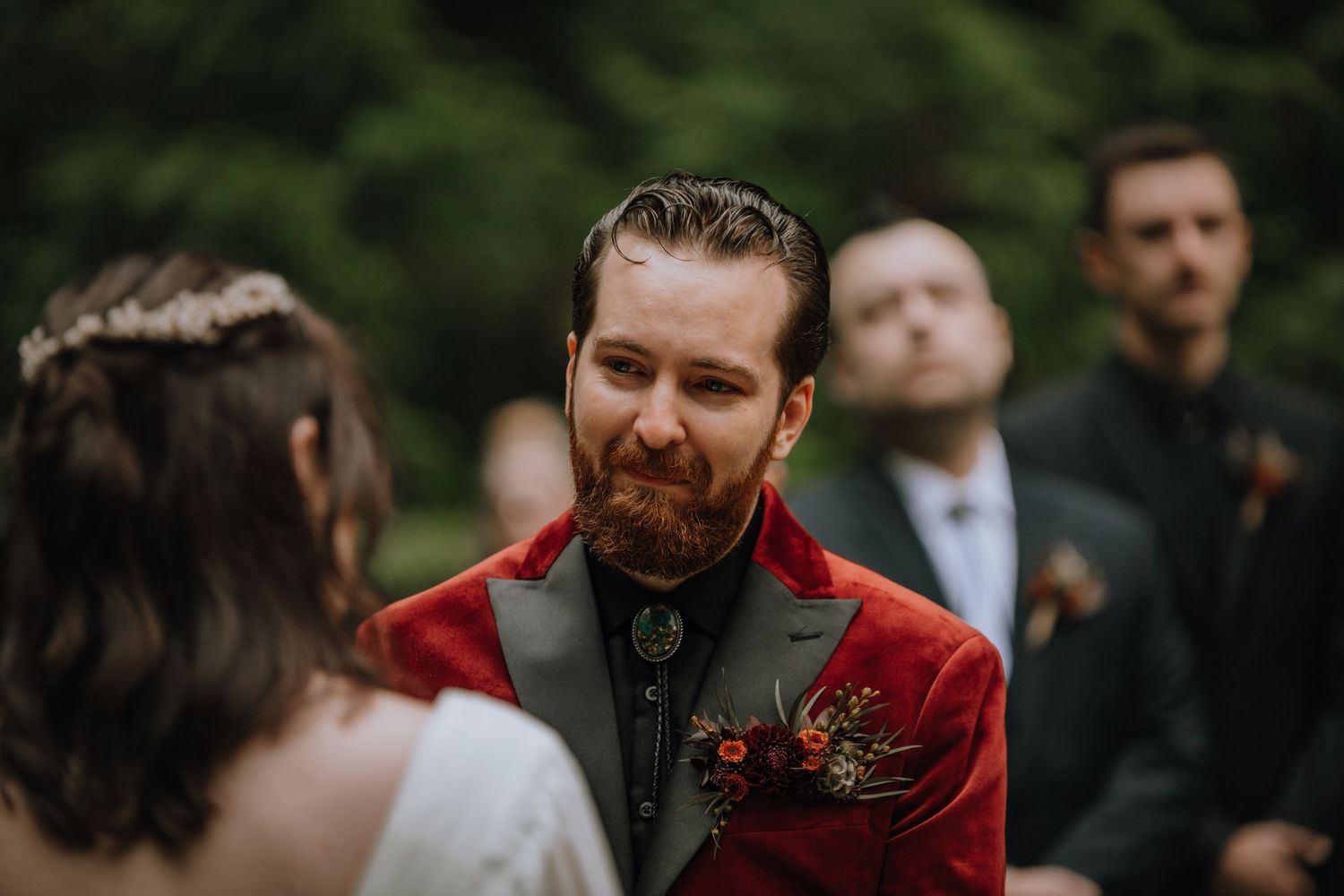 A wedding party celebrates outdoors in a forest setting with warm natural lighting and joyful expressions.