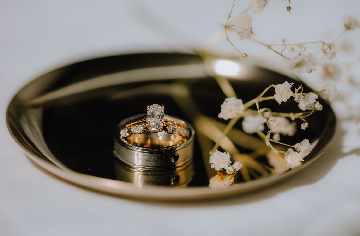 Wedding rings sit elegantly on a gold mirrored tray with delicate white lily of the valley flowers.