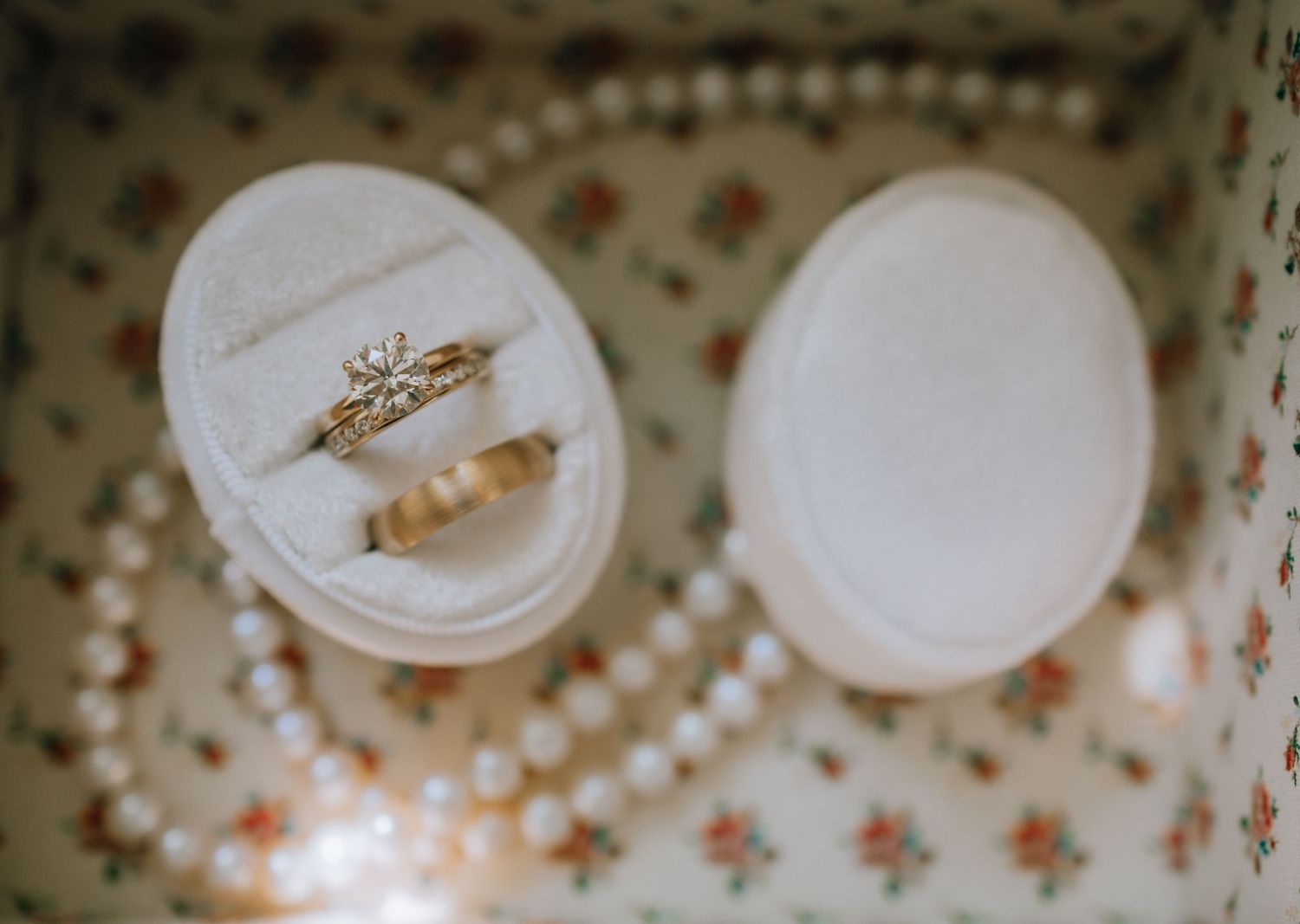 Vintage floral wallpaper pattern with small white plates displaying delicate jewelry pieces arranged in a row.