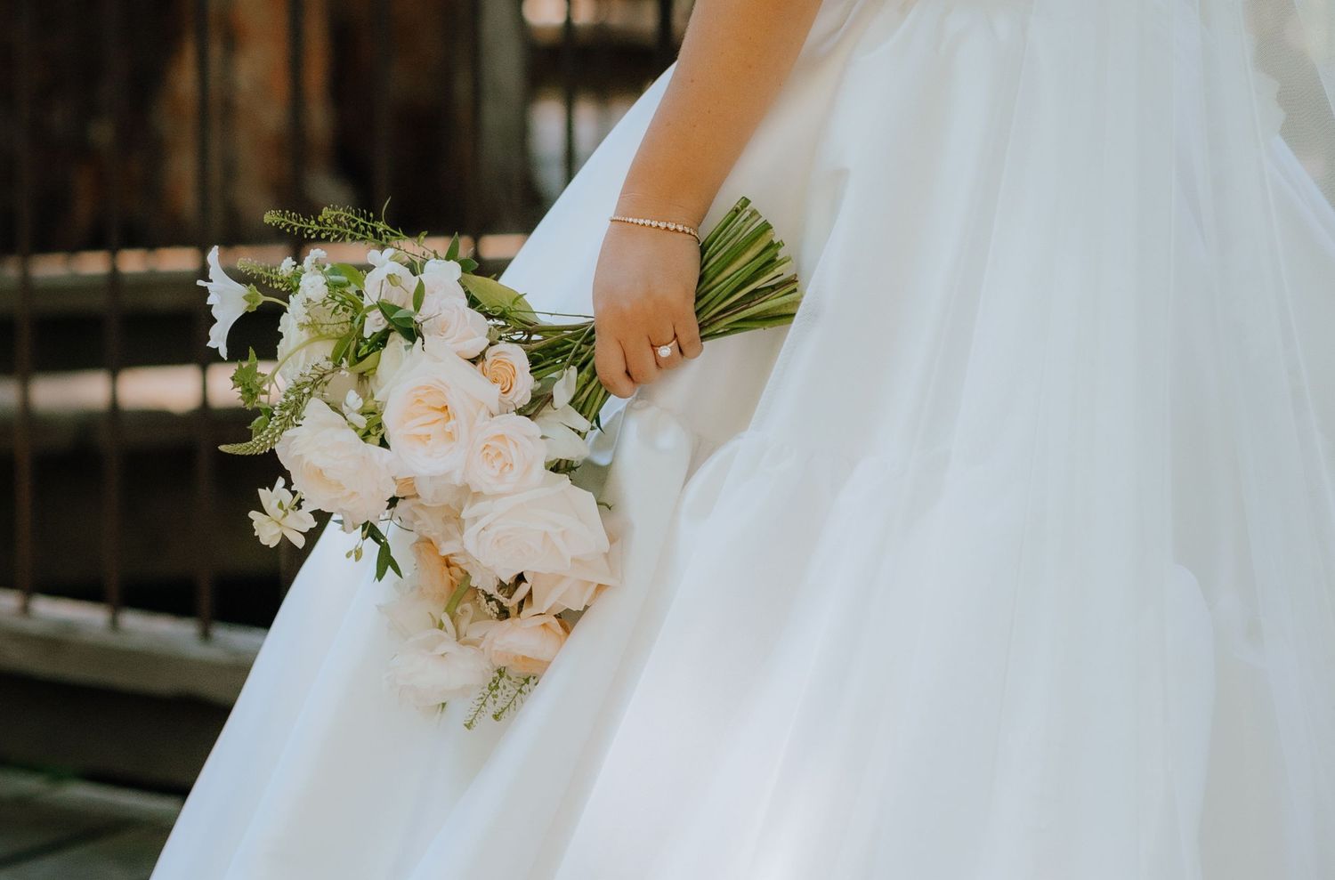 A delicate bridal bouquet of blush pink and white flowers held against a flowing white wedding dress.