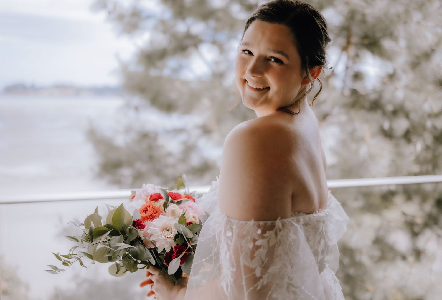A strapless off-shoulder wedding gown adorned with lace as the wearer holds a vibrant floral bouquet.