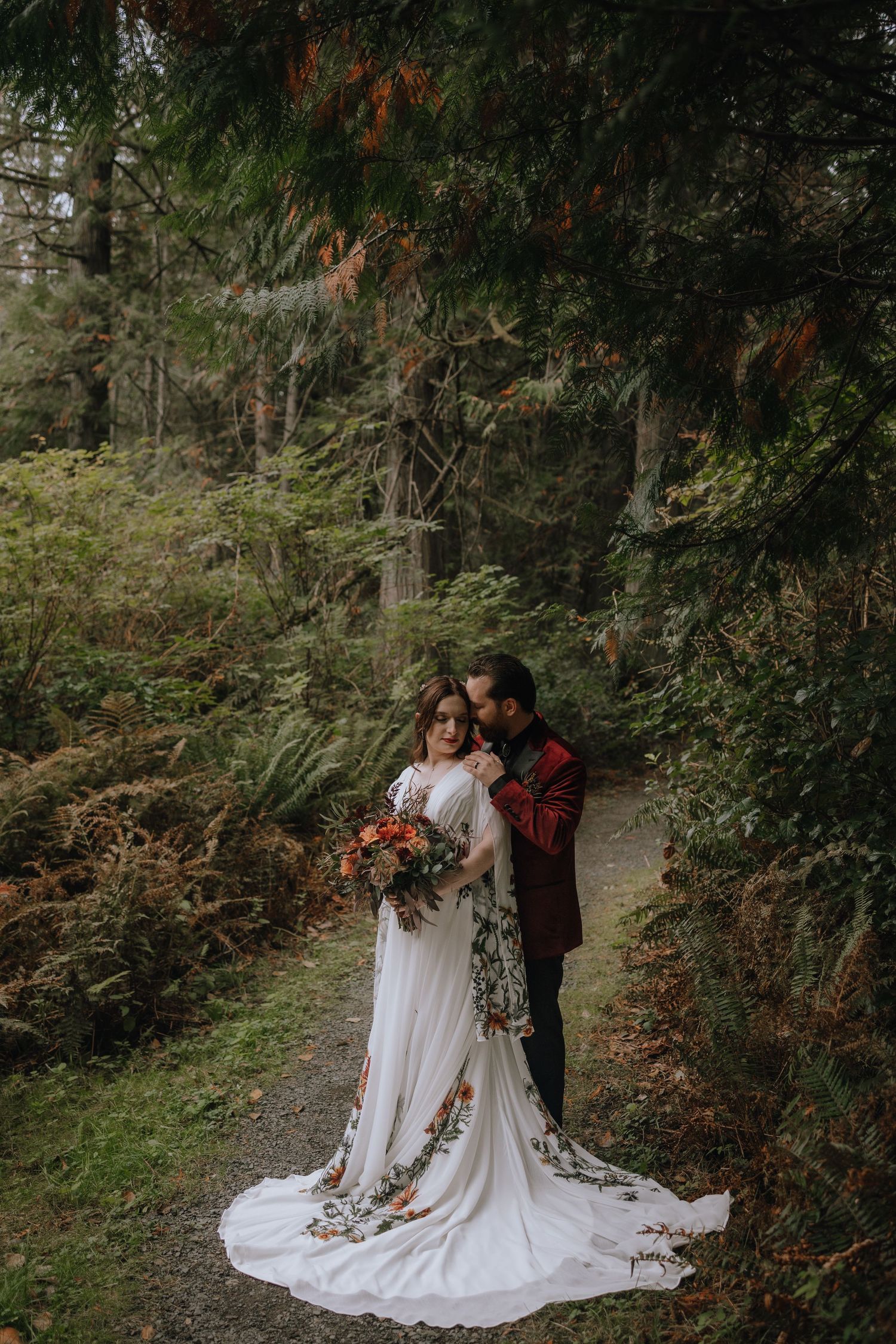 A romantic wedding couple embraces in a lush forest setting with autumn foliage and natural greenery.