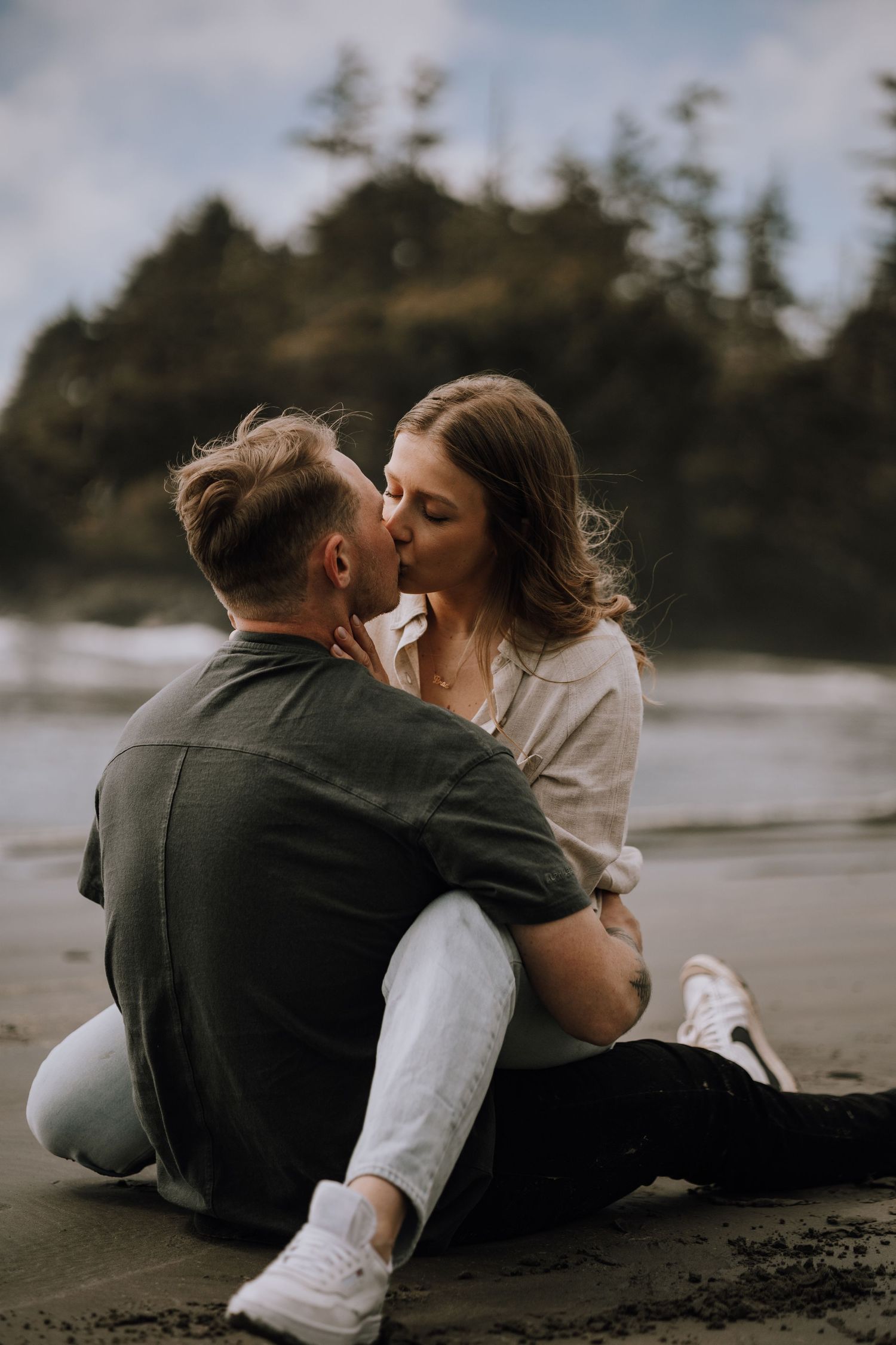 A couple sits on a beach sharing intimate moments in a romantic photoshoot sequence at Cox Bay on Vancouver Island