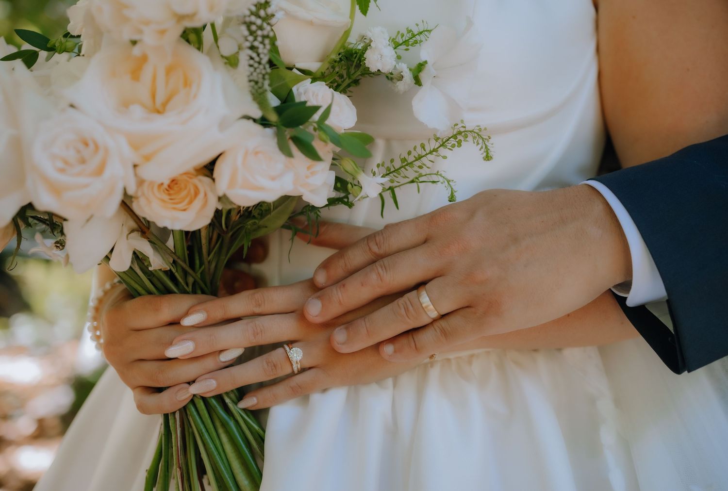 Close-up view of hands holding a white rose wedding bouquet with delicate greenery accents.