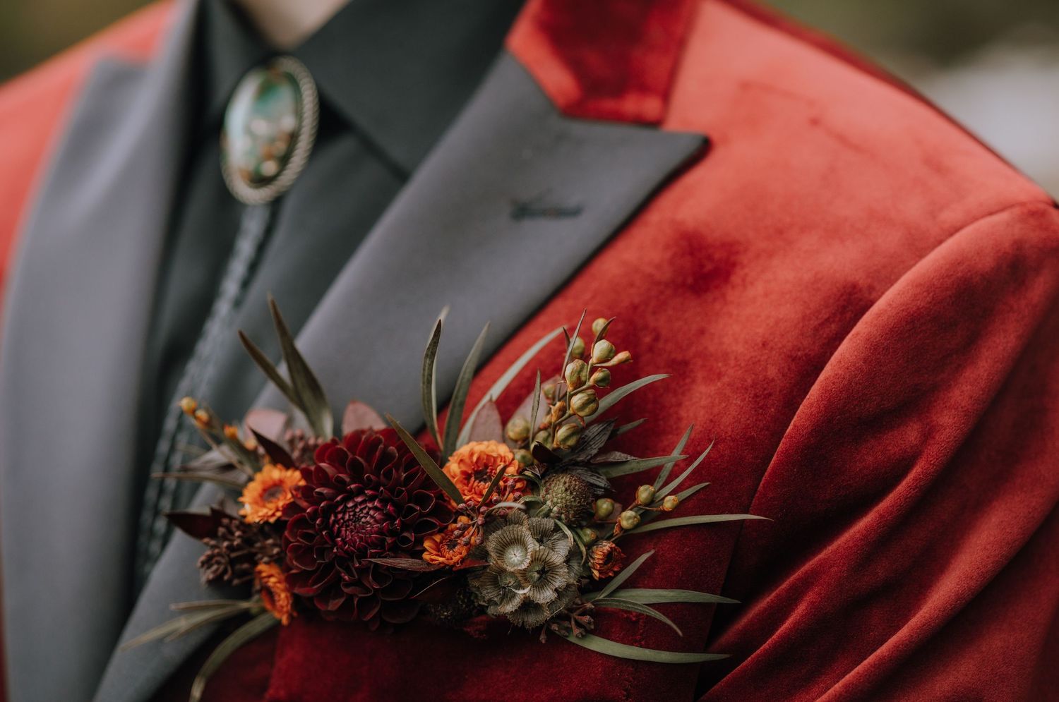 Wedding boutonnieres with red flowers and greenery arranged on a RED suit jacket.