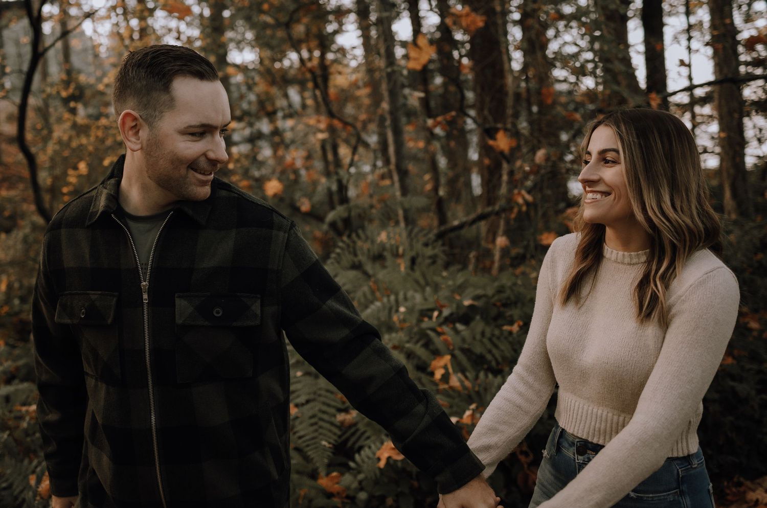 A couple shares a romantic moment while walking through autumn woods with golden-brown foliage.