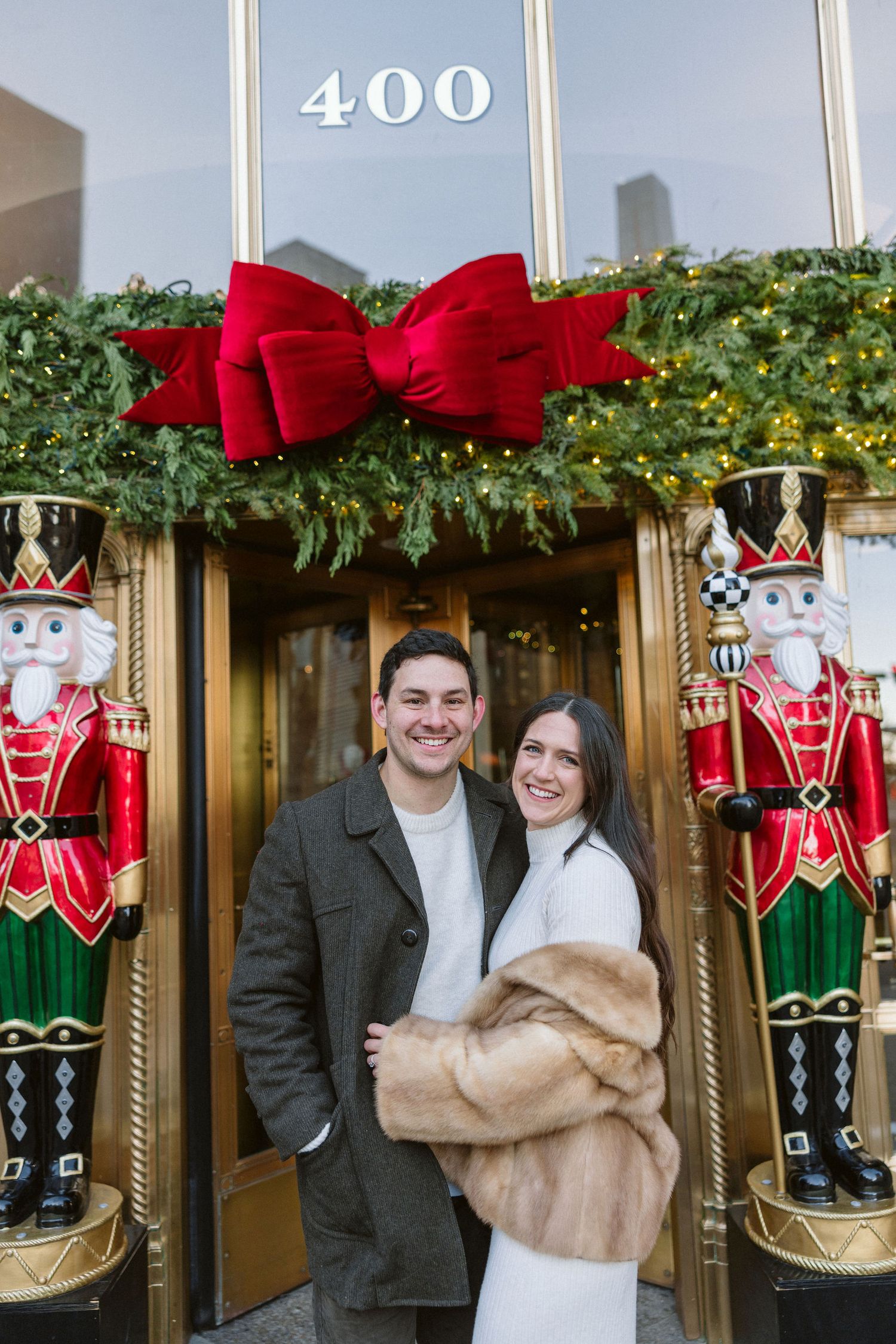 Smiling couple embracing in front of a festive 400 entrance decorated with a big red bow, greenery and two giant nutcracker statues.