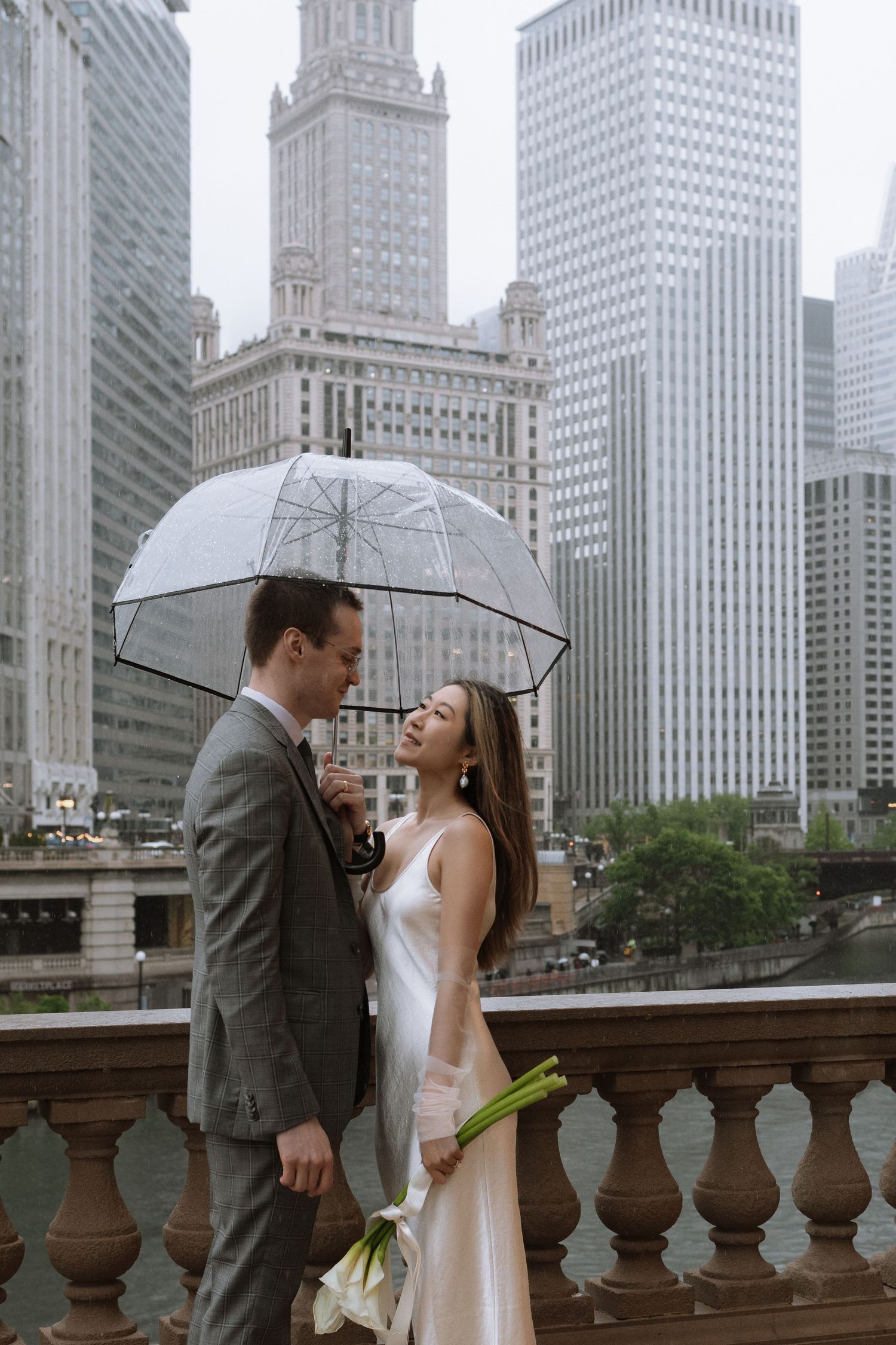 A couple shares an intimate moment under a clear umbrella with Chicago skyscrapers in the background.