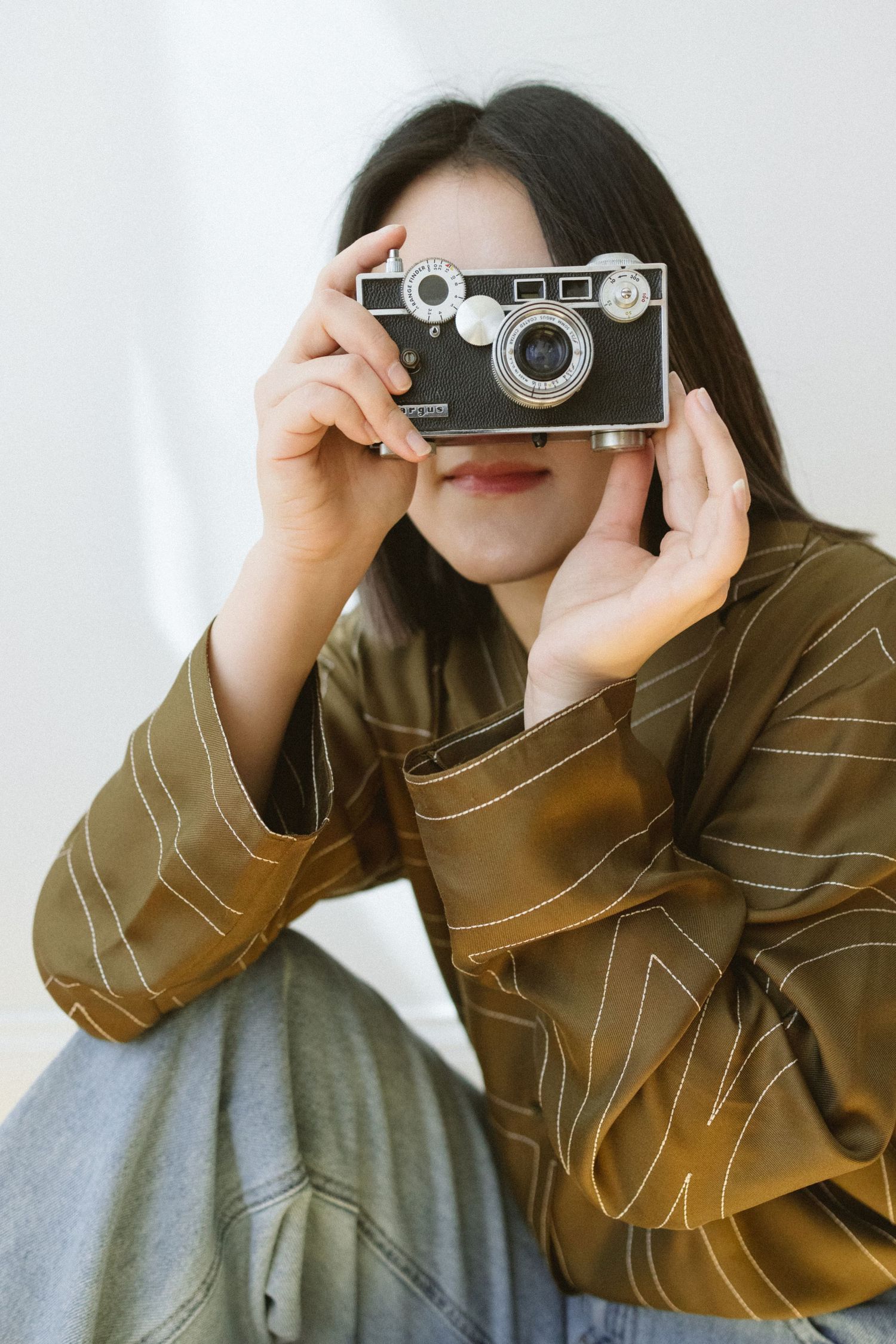 Artistic portrait series of person using vintage camera in brown jacket.