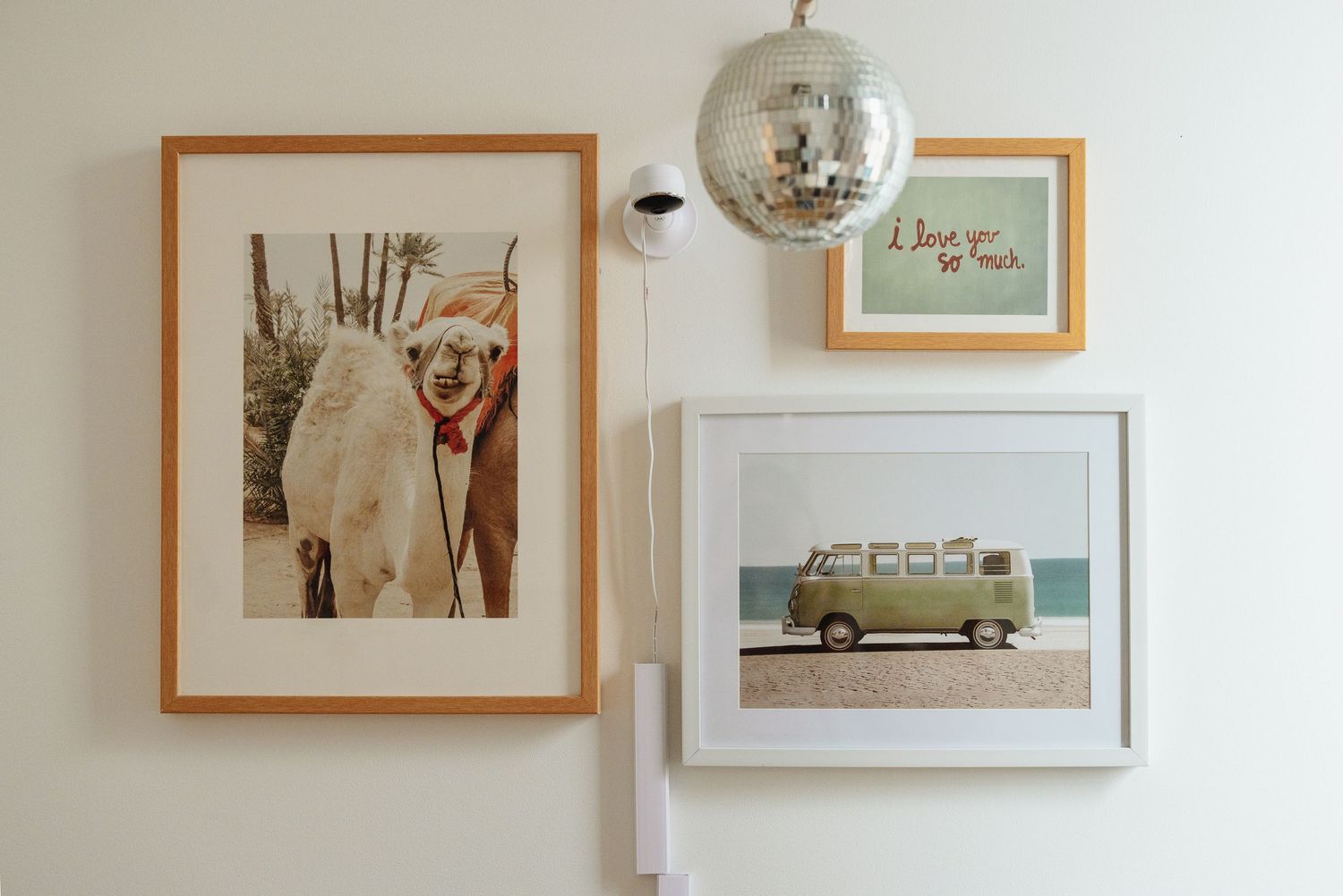 Gallery wall with framed llama photo, vintage VW bus print, love quote art, and a disco ball on white wall.