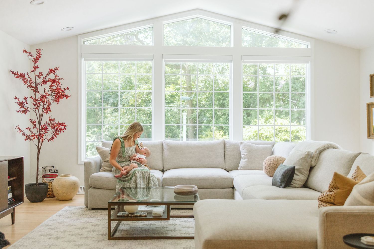Bright modern living room with large cathedral windows, L-shaped beige sectional, glass coffee table and pink floral decor.