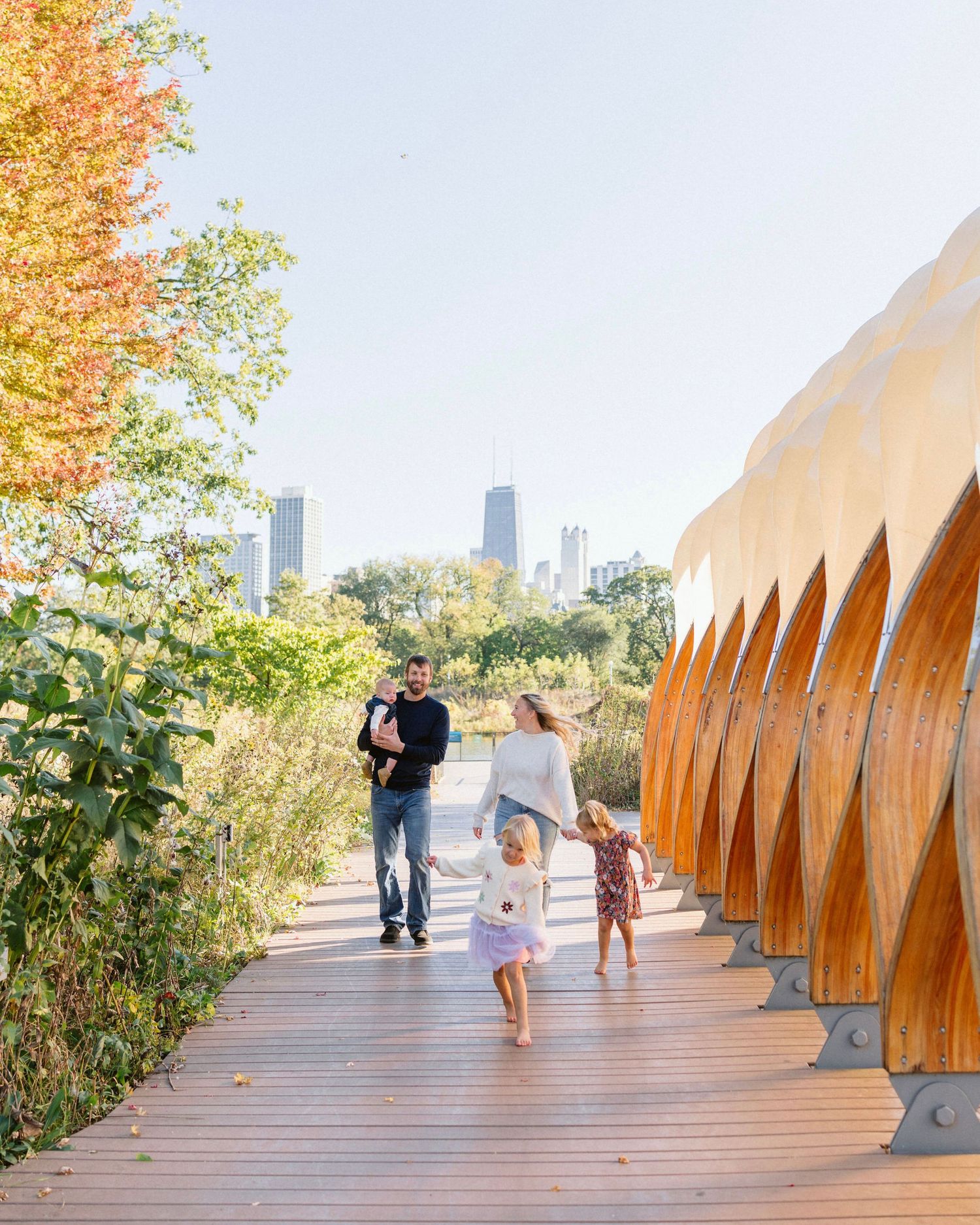 Family walking on a wooden bridge path in Lincoln Park with Chicago skyline in the background on a sunny autumn day.