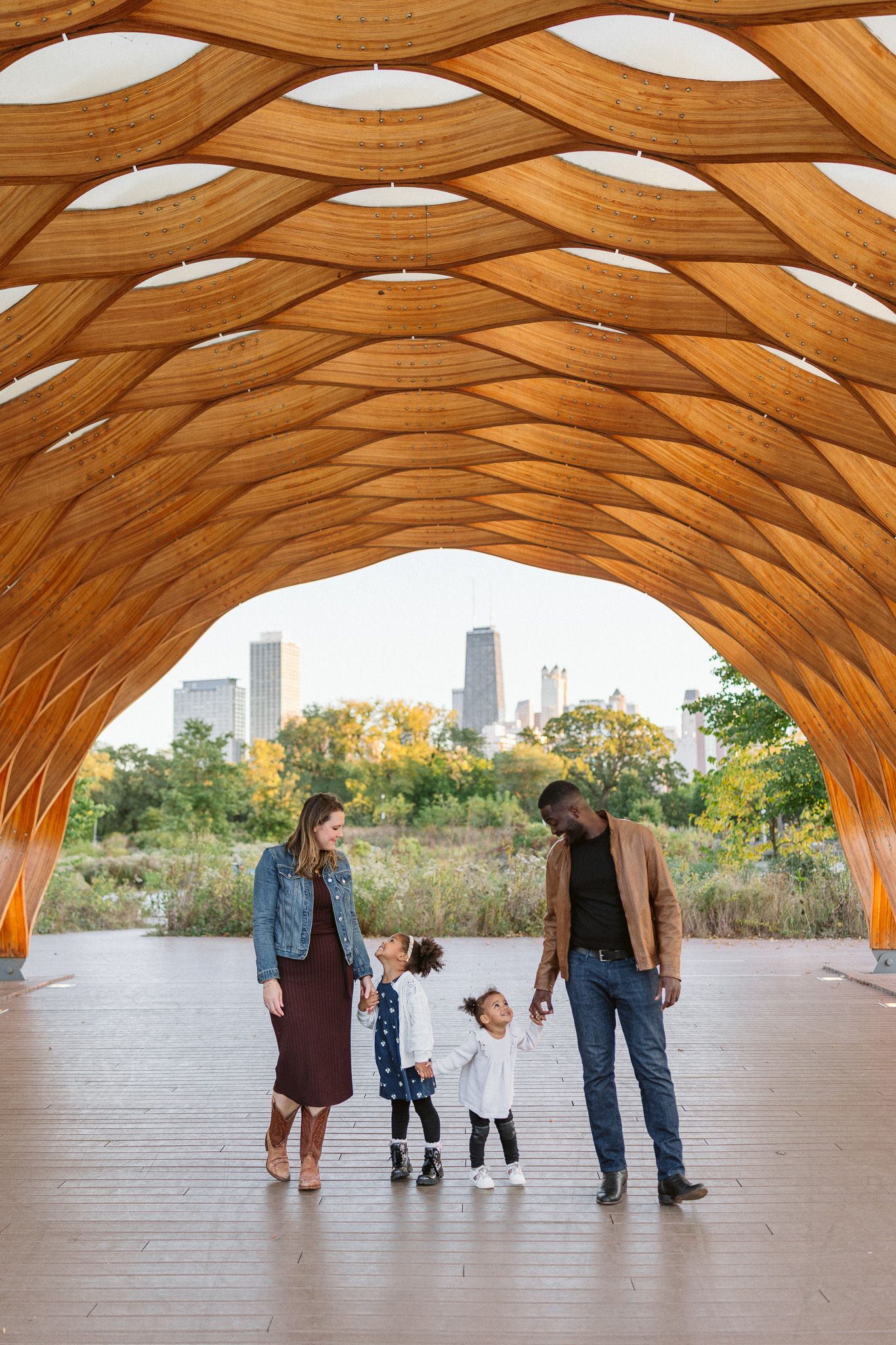 Family of four stands under a stunning wooden lattice pavilion in Chicago's Lincoln Park with city skyline in background.