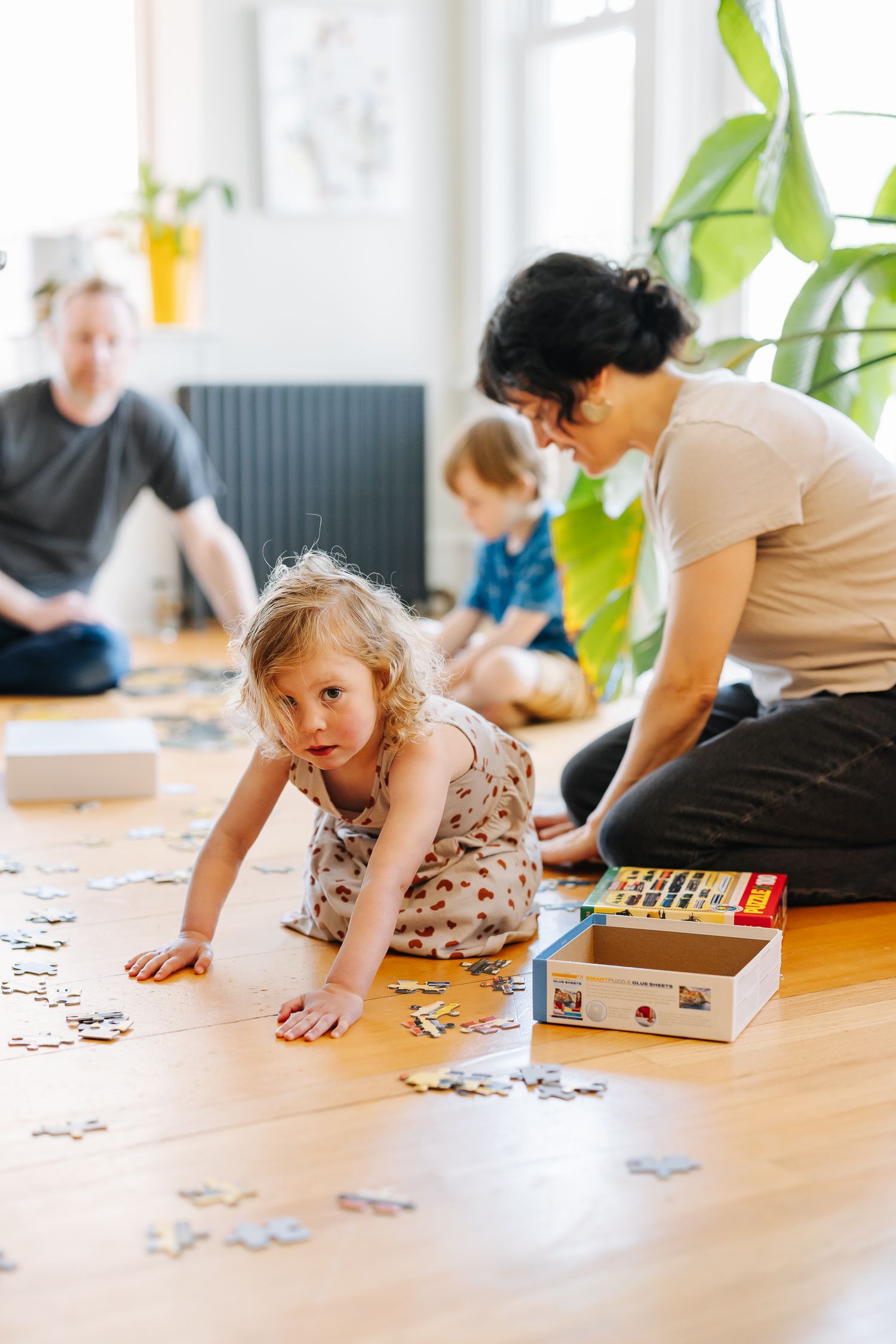 People working on a jigsaw puzzle together on a wooden floor with natural lighting.