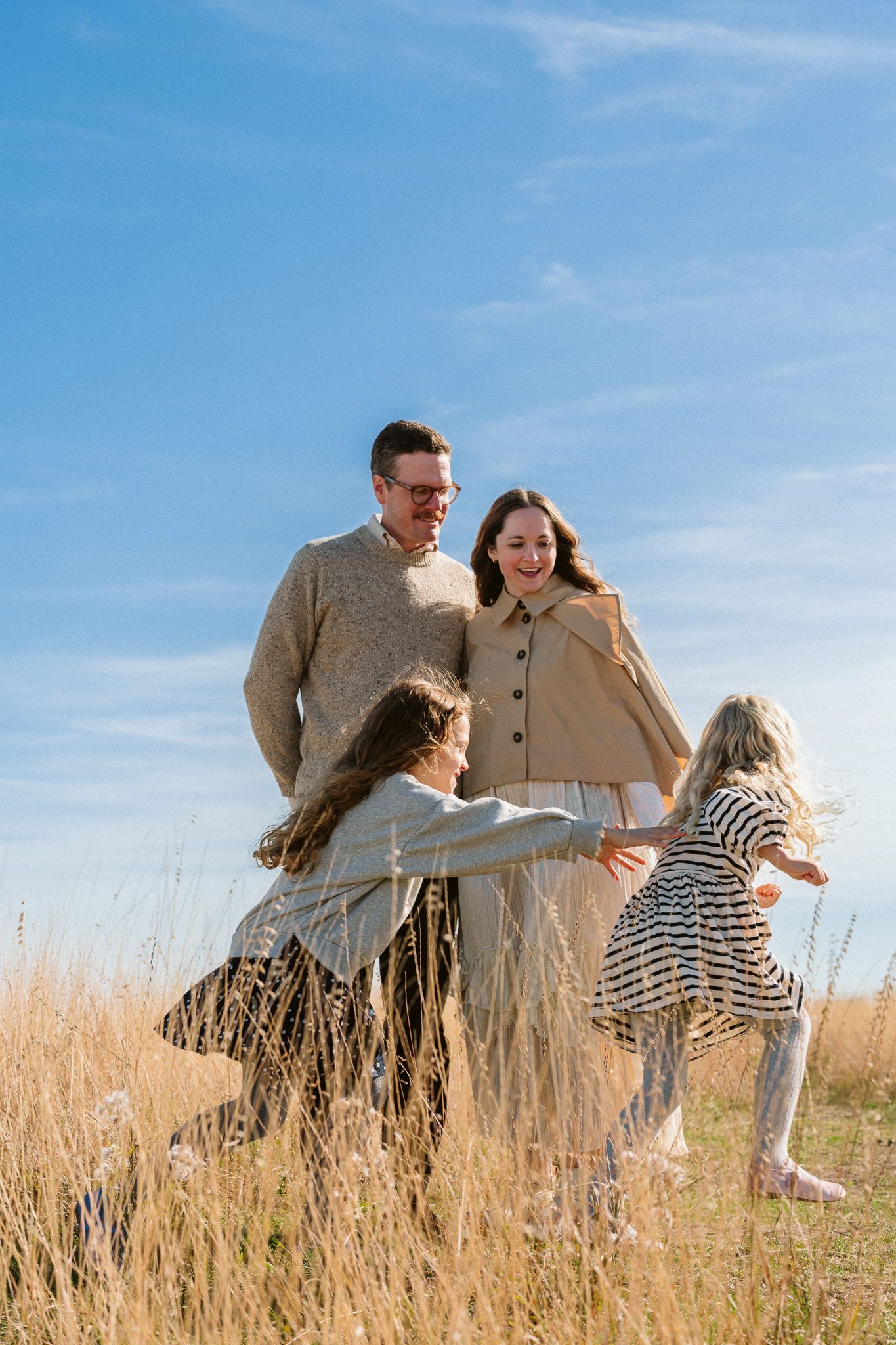 Happy family with two daughters playing in a golden field under a bright blue sky on a sunny day.