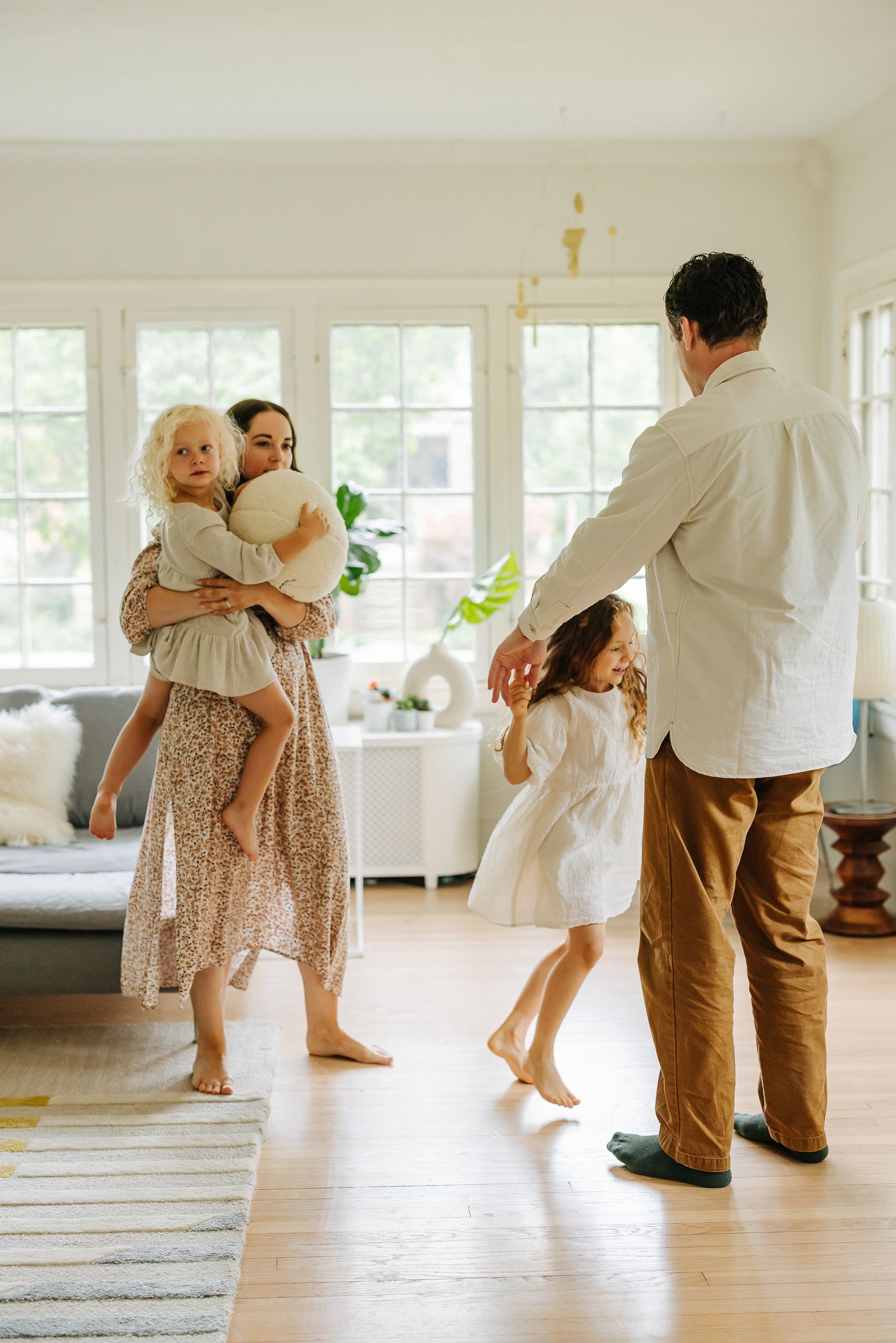 A family dancing together in a bright, modern living room with hardwood floors.