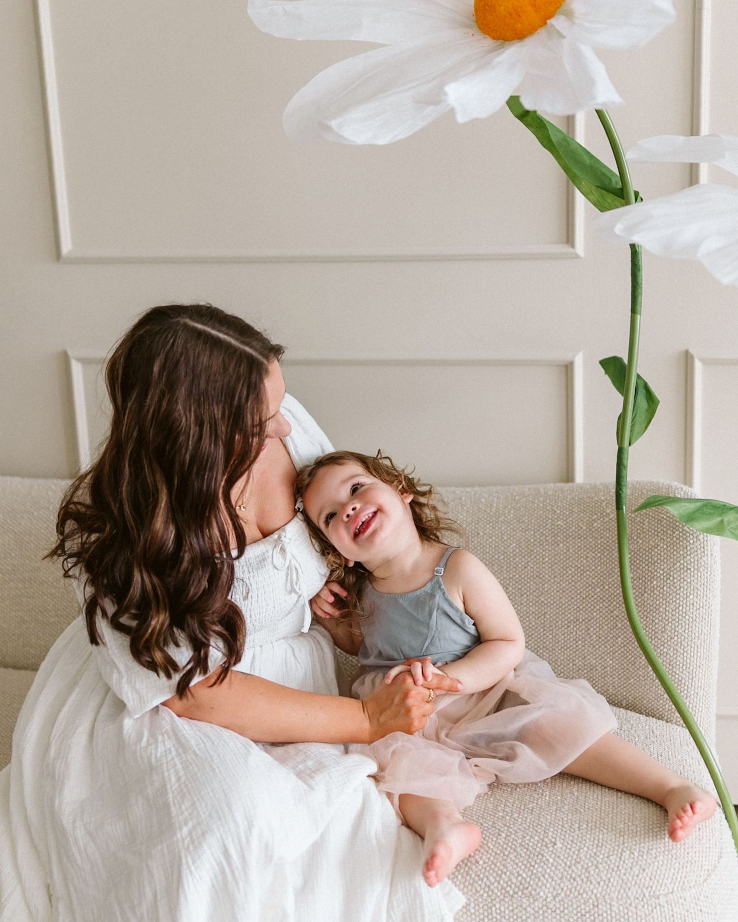 A tender moment shared between parent and child on a white couch with floral decor in the background.