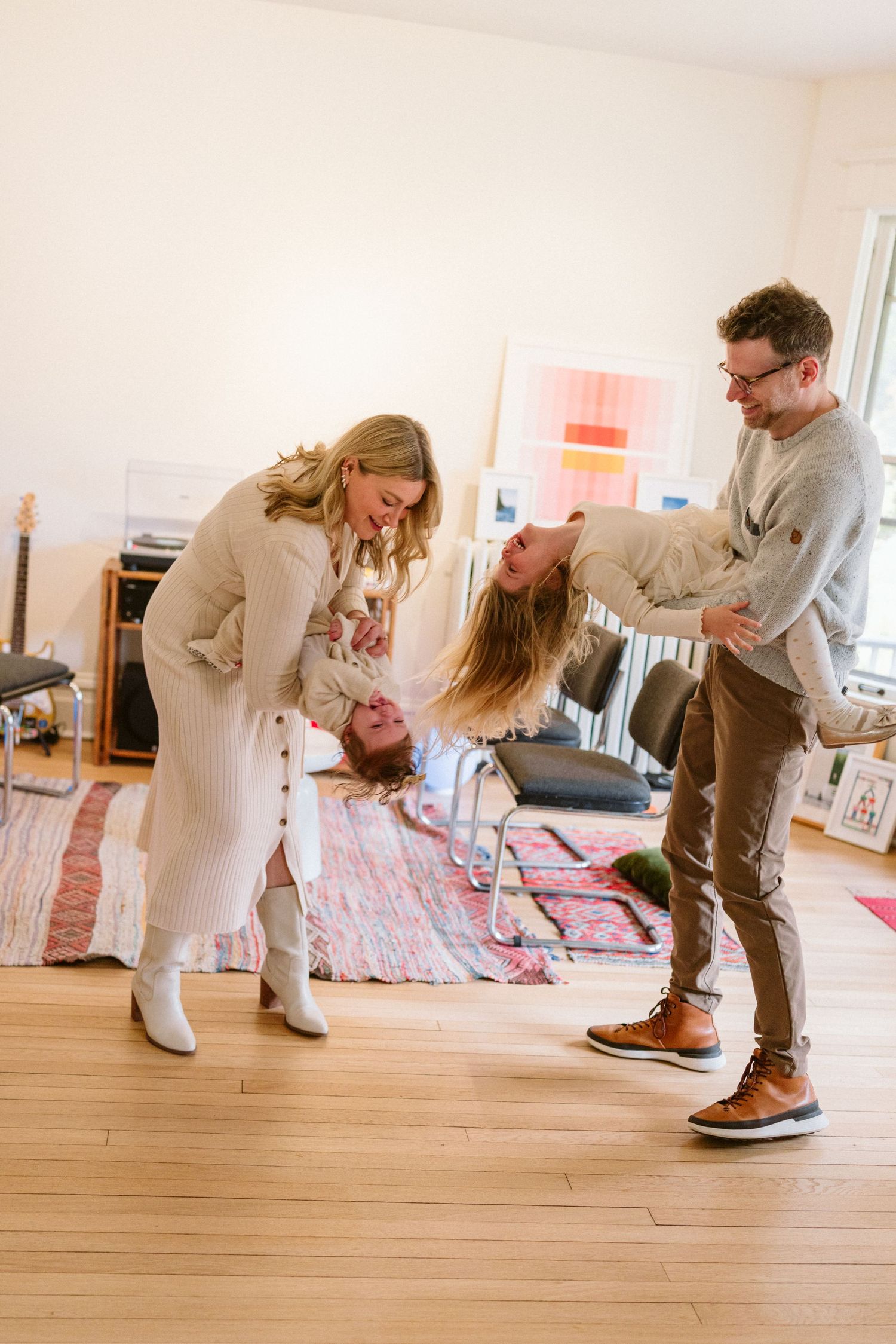 A joyful family plays together in a bright living room, with parents swinging a laughing child upside down.