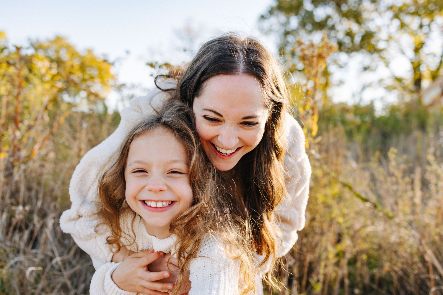 Two people share a joyful moment outdoors in autumn with golden sunlight filtering through trees and leaves.
