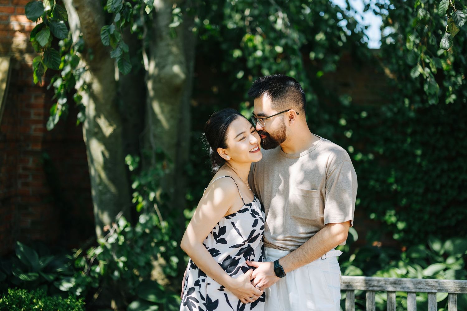 Intimate couple photoshoot under lush green trees in outdoor garden setting.