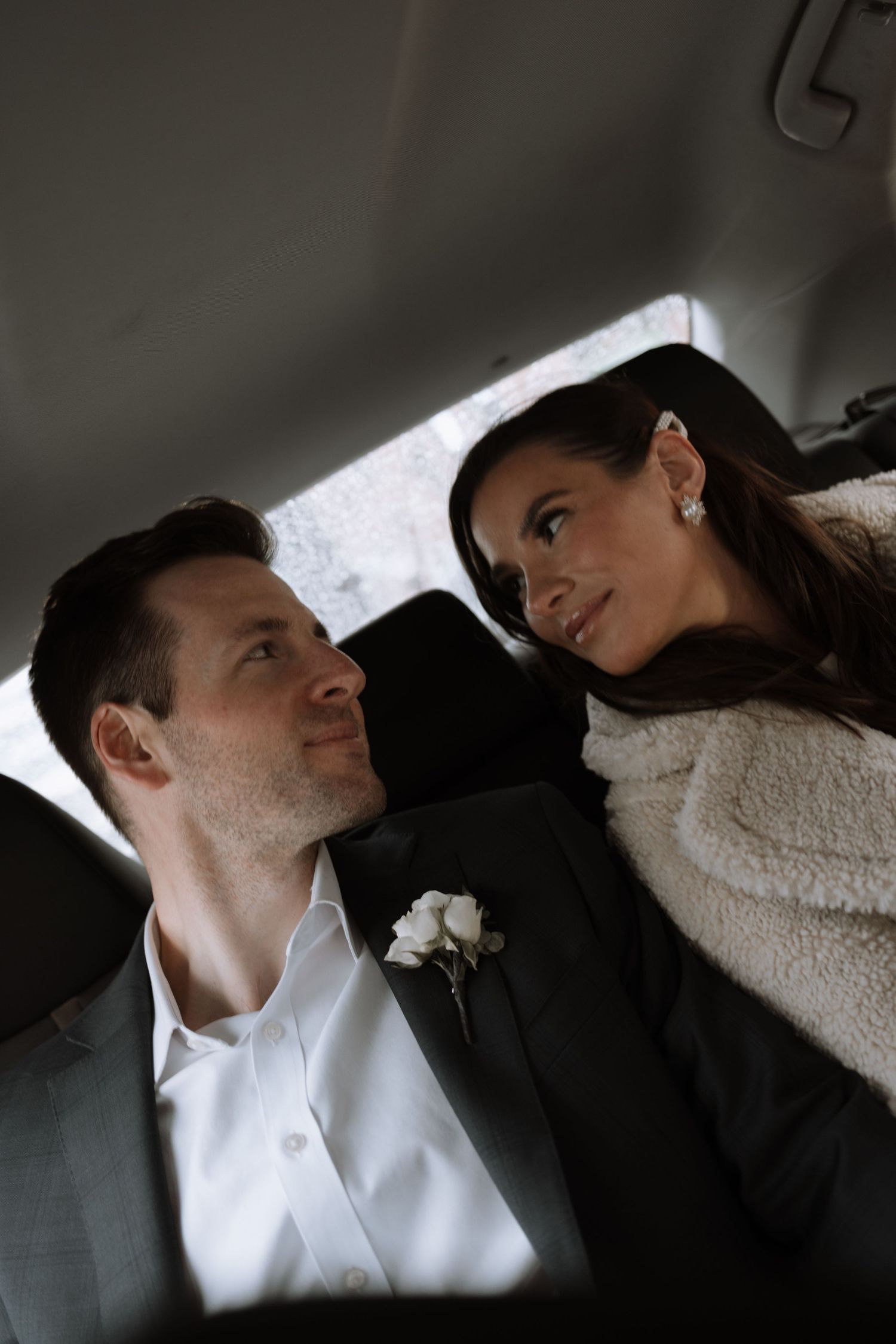 A couple sitting close together in the backseat of a car share an intimate moment.