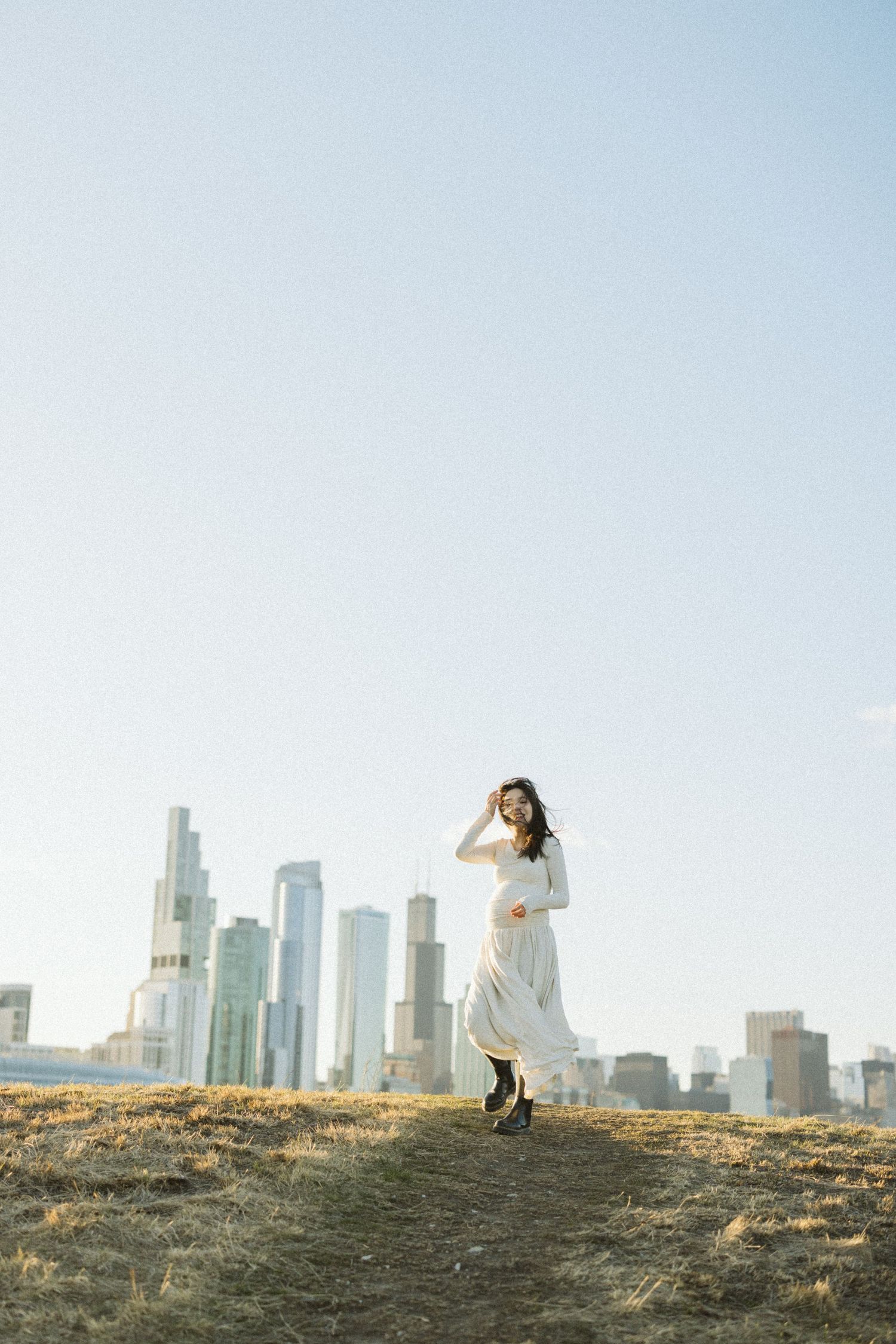 Woman in a flowing white dress stands on a hilltop against a backdrop of downtown Los Angeles skyscrapers.