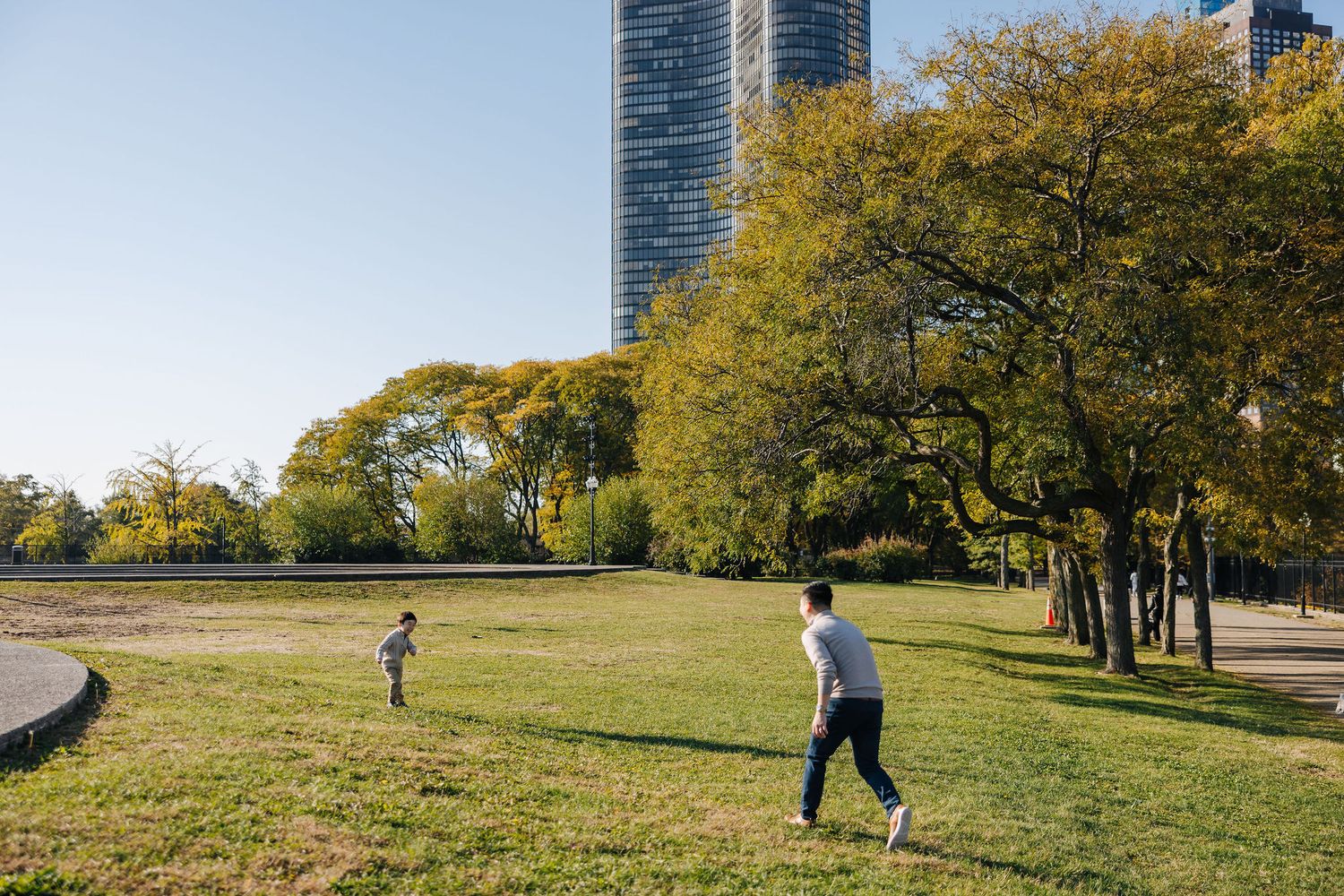 Two people playing in a sunny urban park with lush green trees and a modern skyscraper in the background.