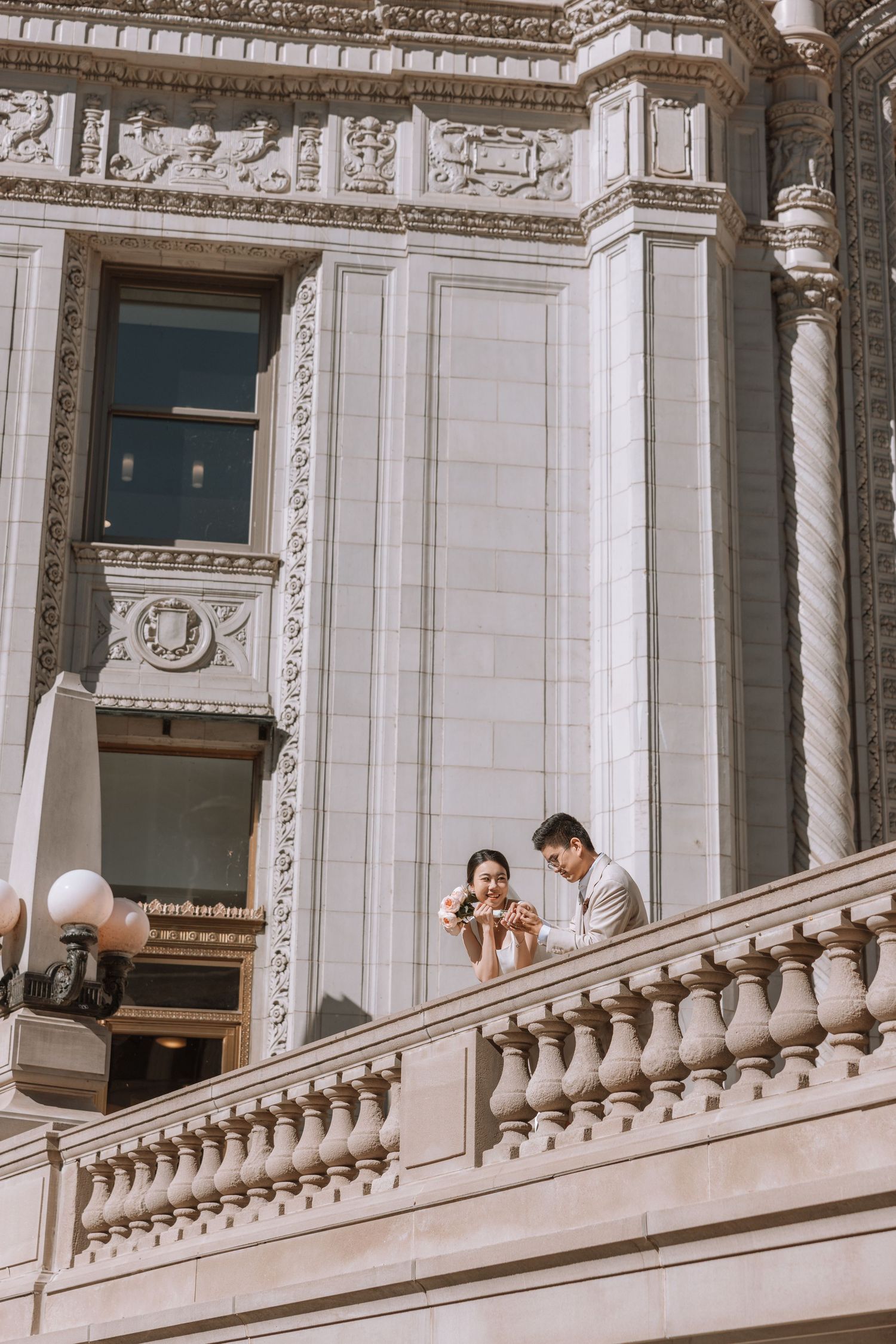 Two people conversing on an ornate white stone balcony with classical architectural details and decorative balusters.