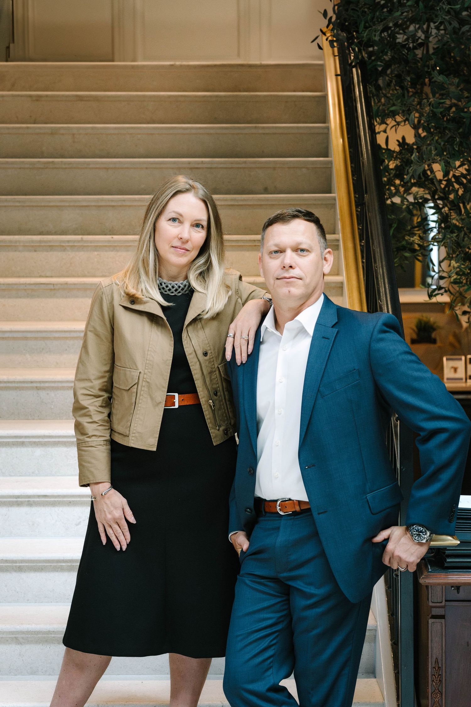 Stylish couple photoshoot on grand staircase combining business and casual wear.
