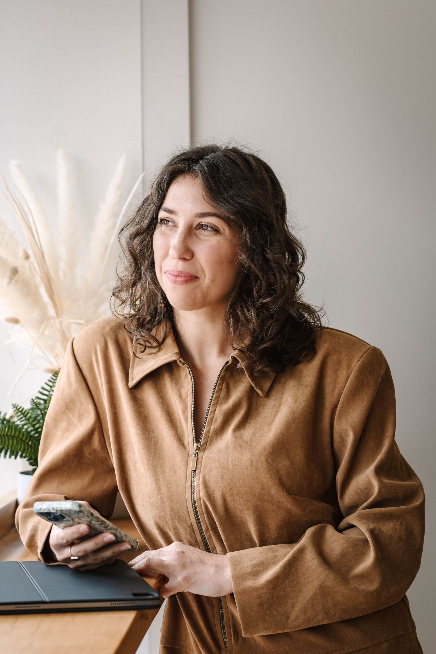 Lifestyle portraits in tan leather jacket against neutral background with dried pampas grass decor.
