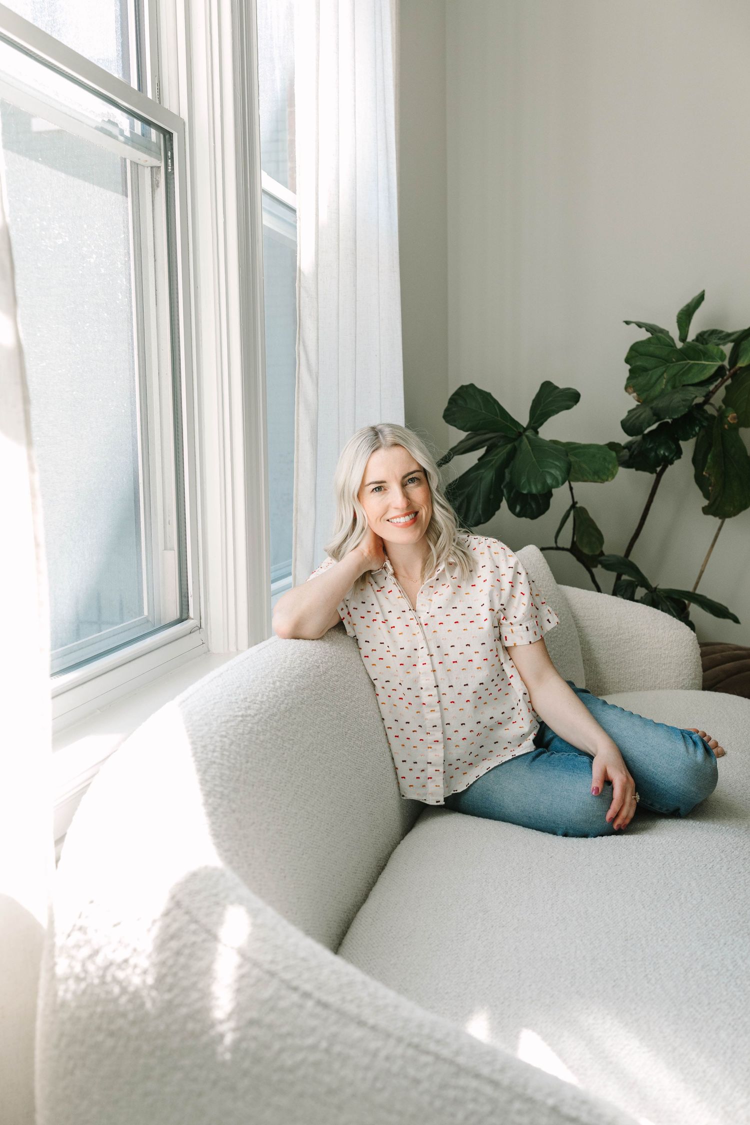 Casual portrait of person relaxing on white couch near window with plant.