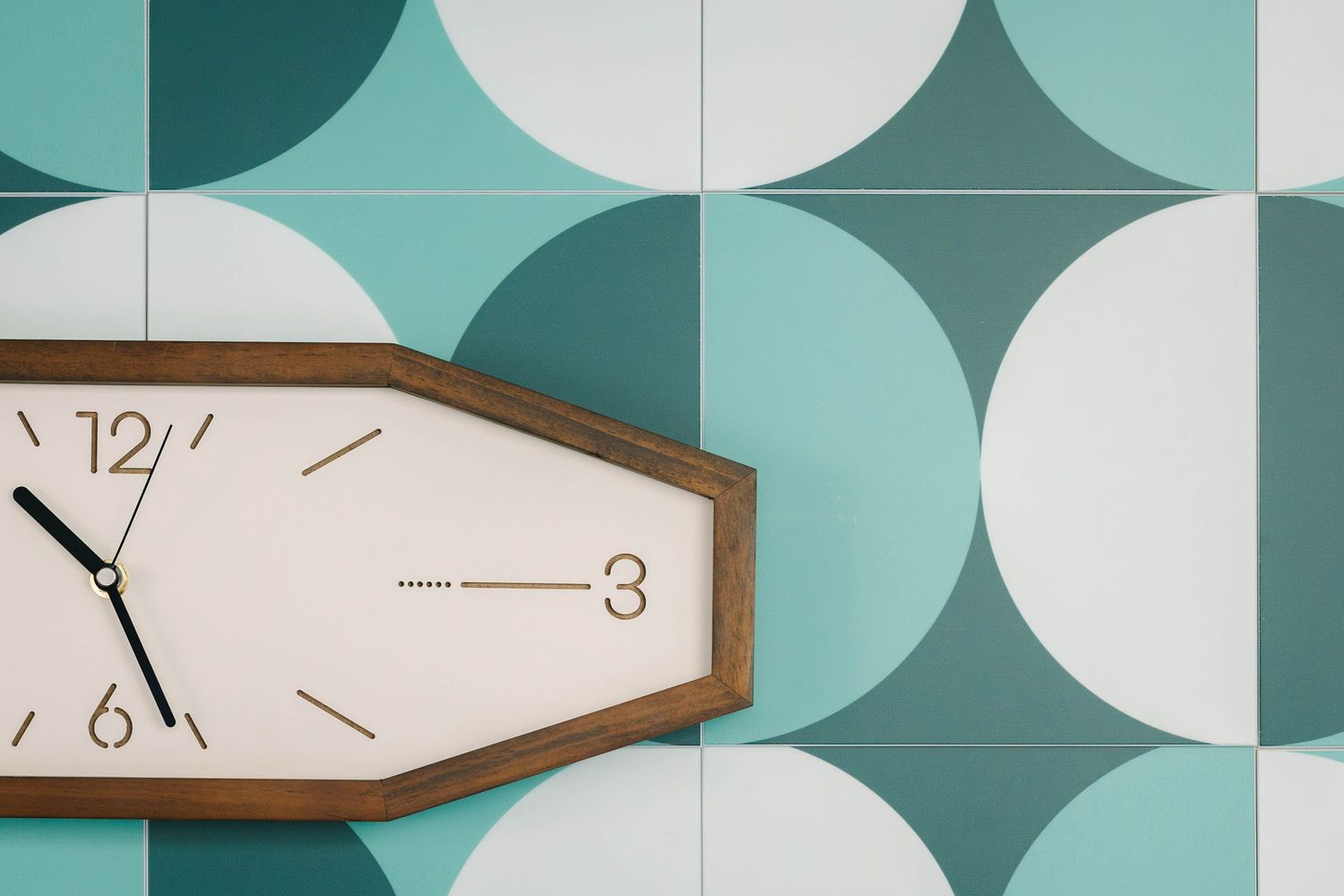 Retro wooden wall clock displaying 11:58 against a teal and white geometric circle patterned tile background.